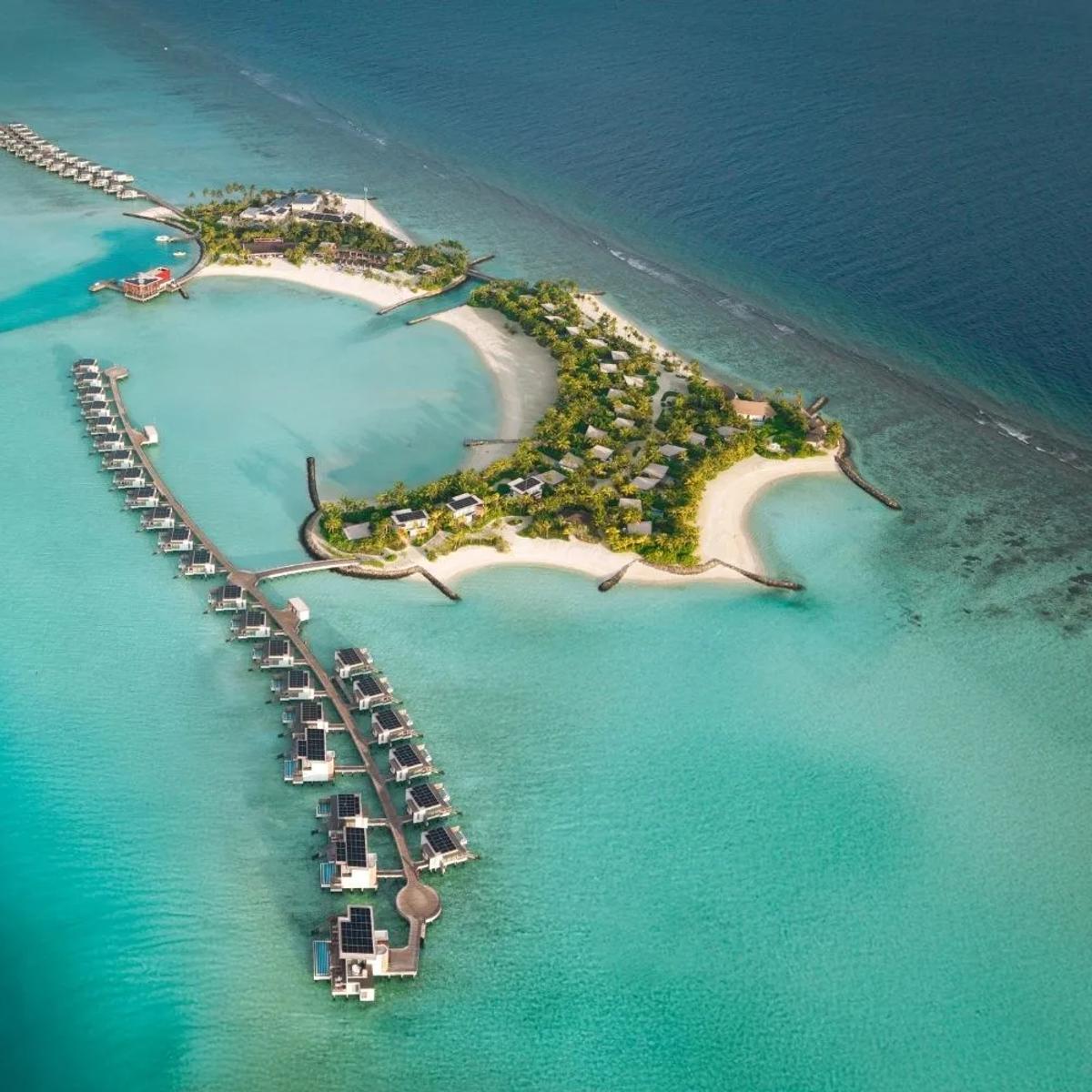 Aerial view of SO/ Maldives' island in Emboodhoo Lagoon, its two rows of overwater villas reaching out from either side of the island and the reef's edge tracing the horizon beyond