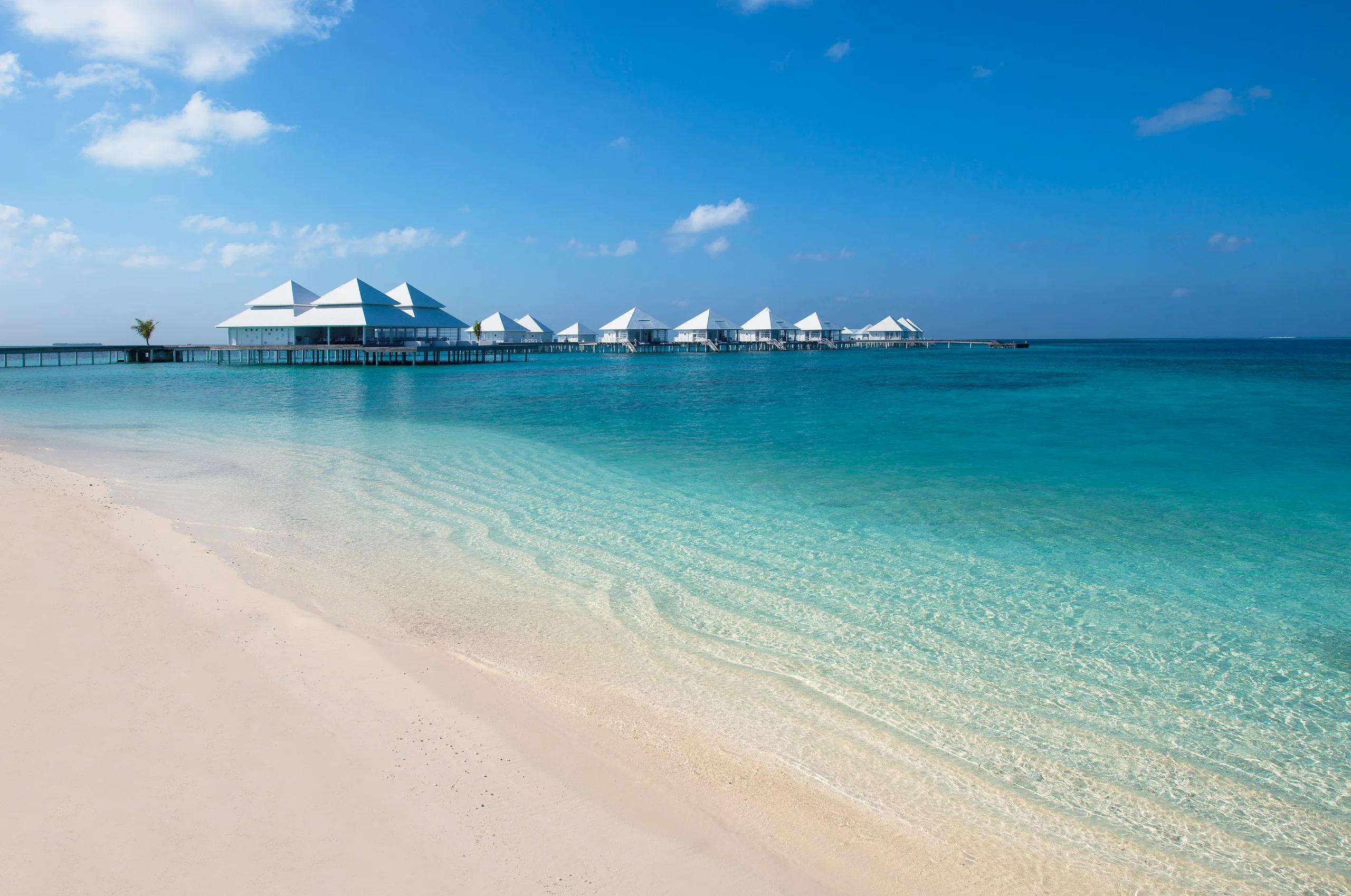 The beach at Diamonds Thudufushi with its white-roofed overwater villa jetty reaching out across the lagoon