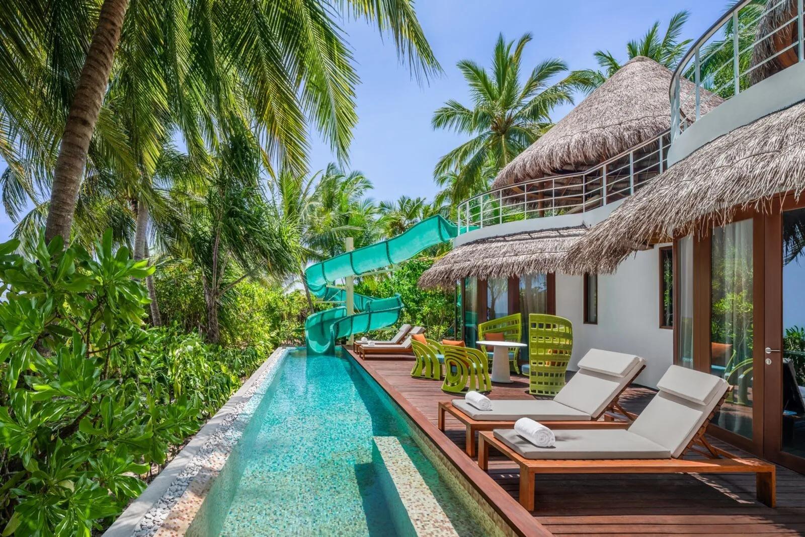 A two-storey Oasis Beach villa at W Maldives with a water slide running from the upper deck into the villa's private pool
