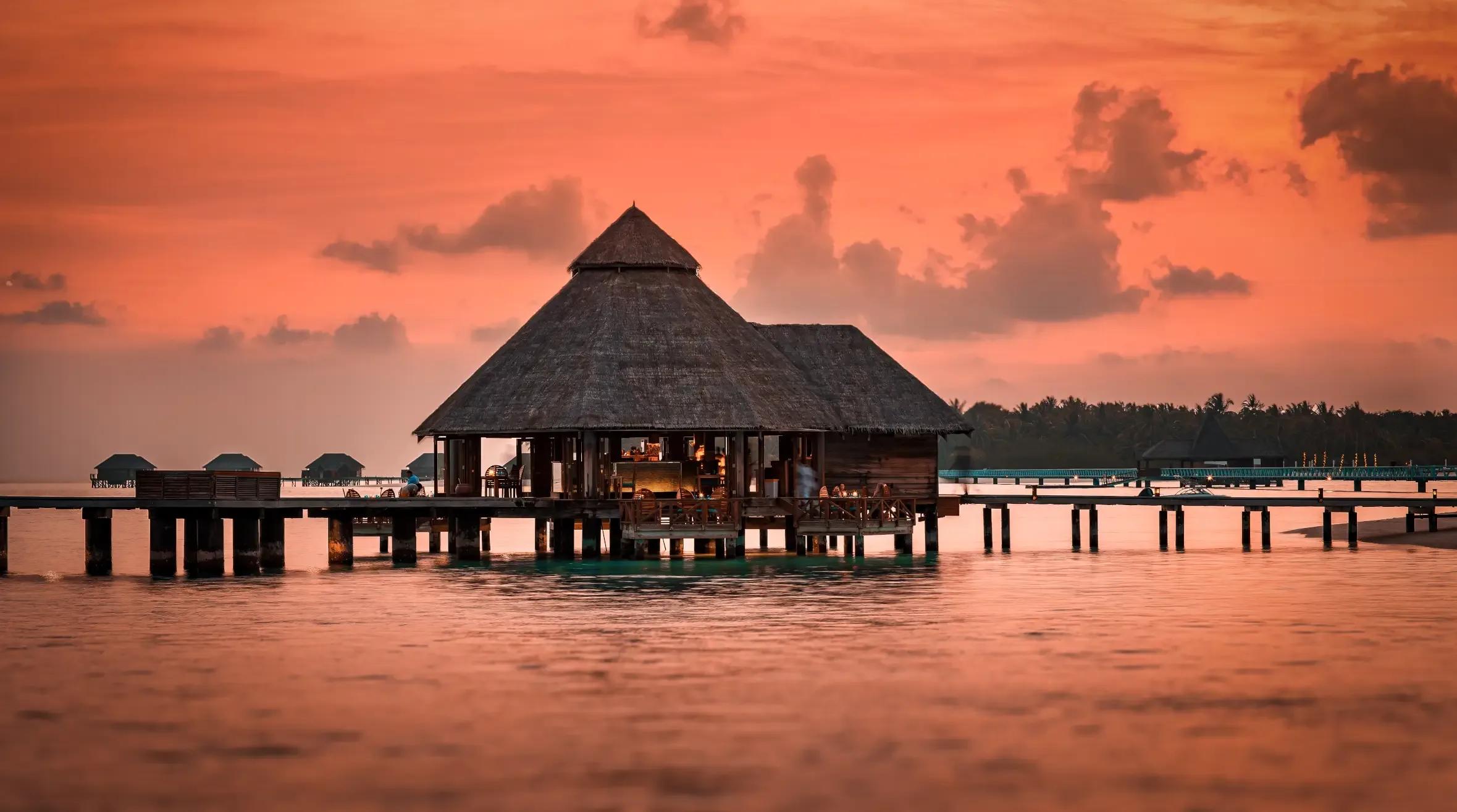 Sunset Grill's thatched overwater pavilion silhouetted against an orange sky at dusk