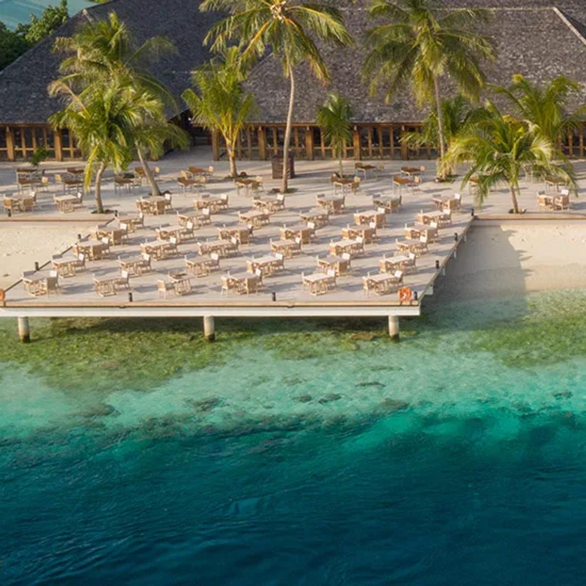 Aerial view of Vilamendhoo's twin overwater sun-deck platforms above the house reef, with a paddleboarder crossing the lagoon