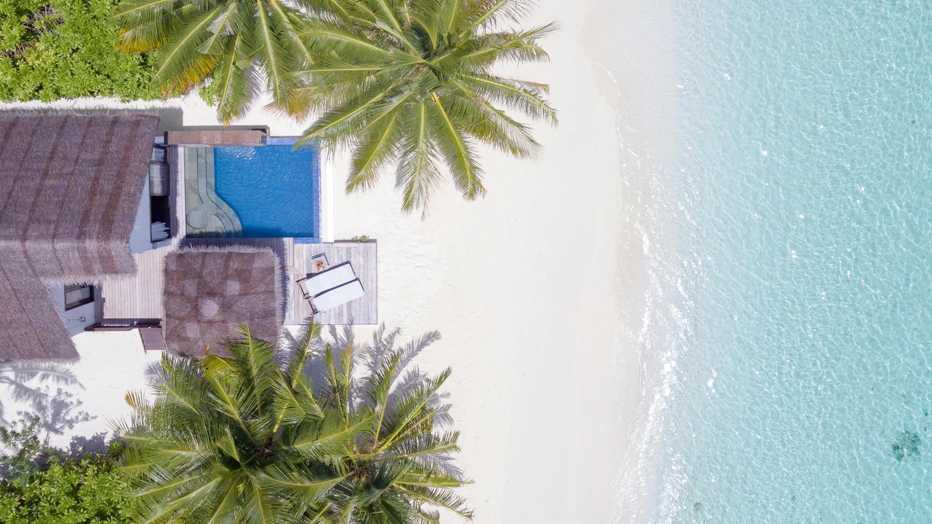 Aerial view of a private plunge pool on a villa deck meeting the white sand and turquoise lagoon at Bandos