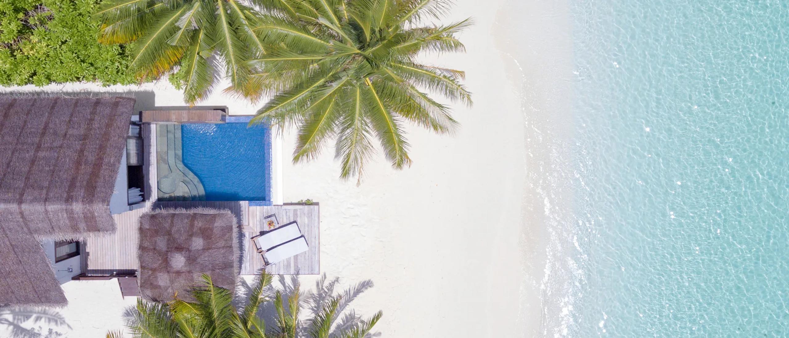 Aerial view of a private plunge pool on a villa deck meeting the white sand and turquoise lagoon at Bandos