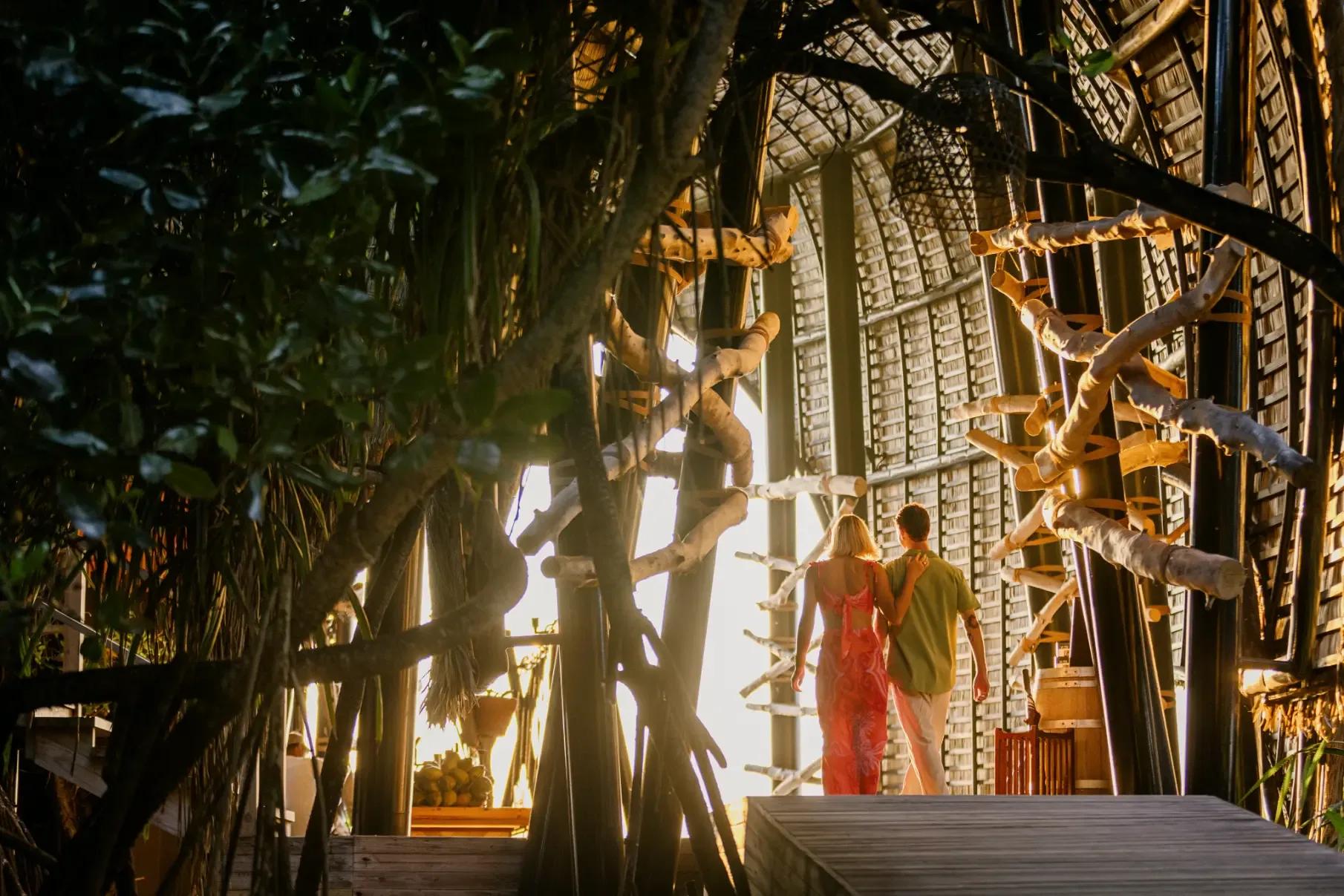 A couple walking arm in arm through Haali Bar's woven bamboo tunnel toward the sunset