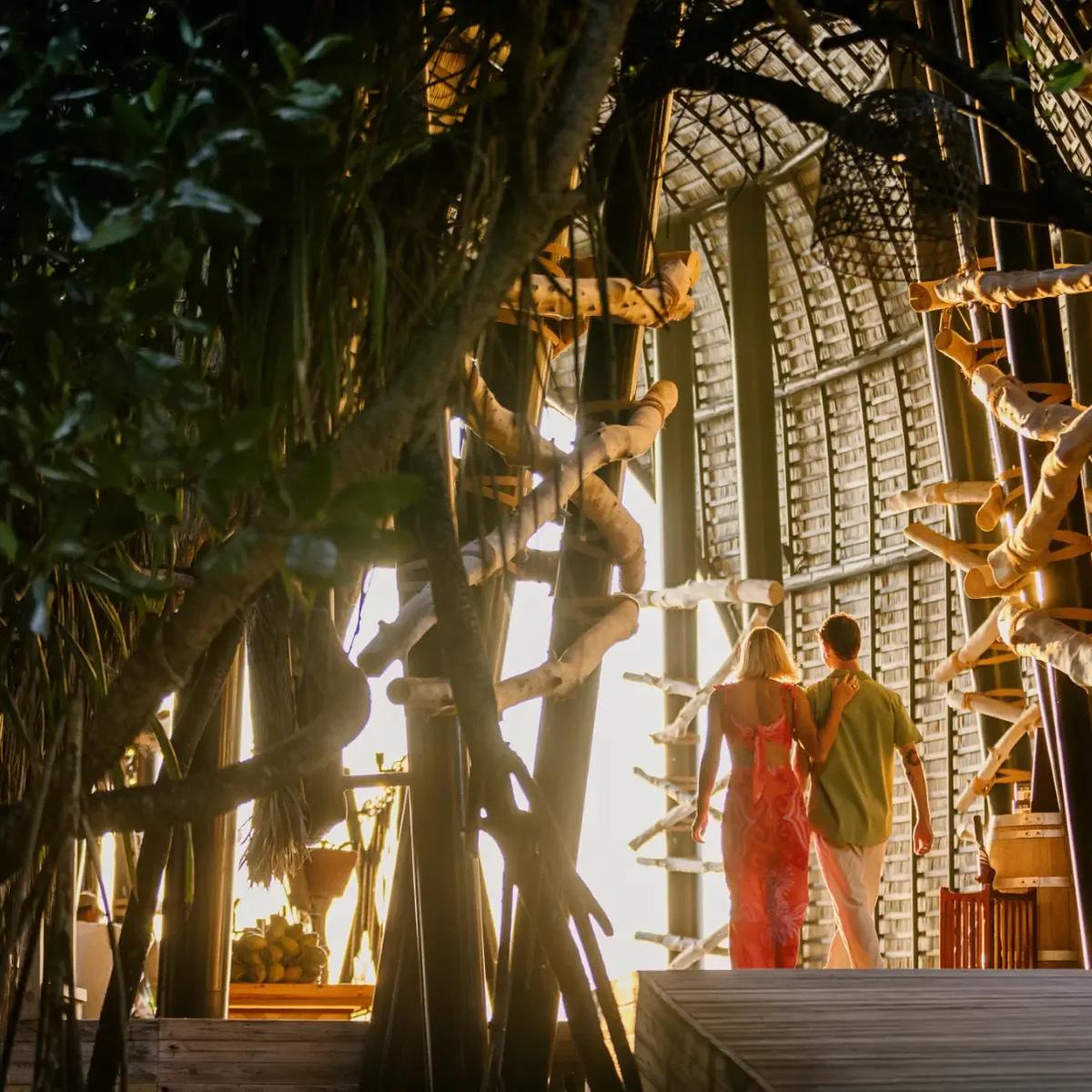 A couple walking arm in arm through Haali Bar's woven bamboo tunnel toward the sunset