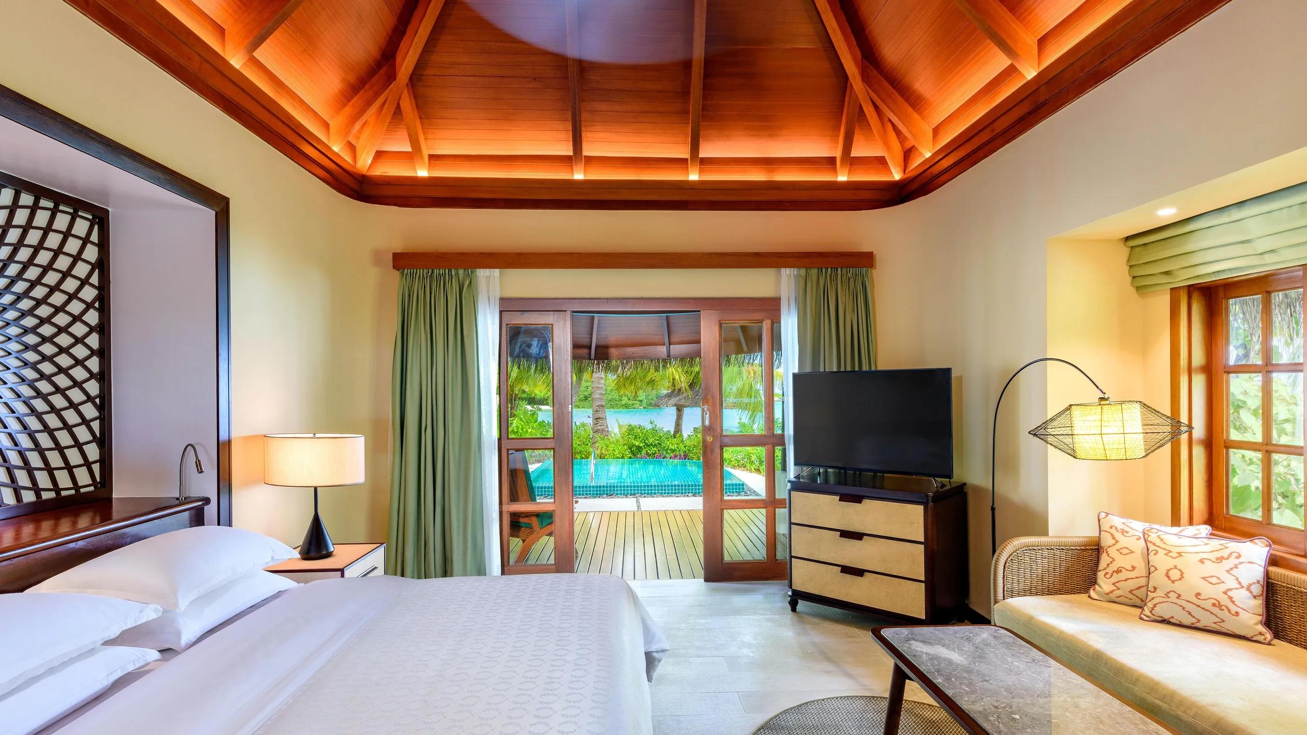 Inside a Cottage villa bedroom, with glass doors opening onto its private plunge pool deck