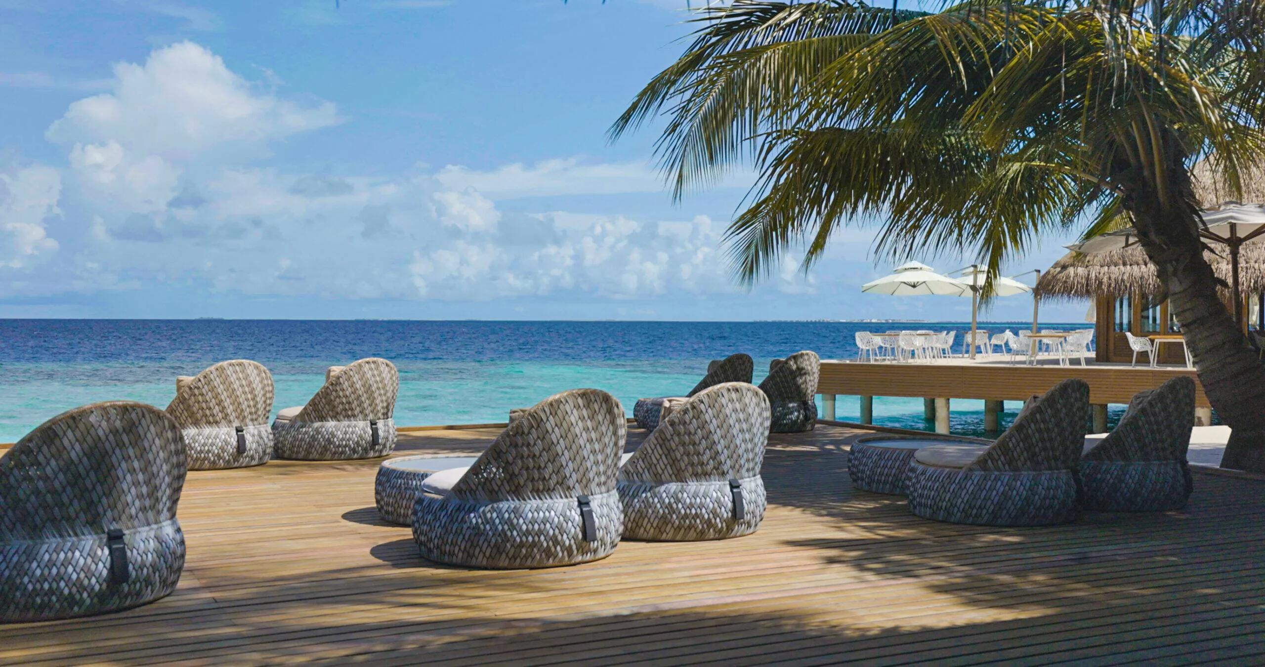 Woven daybeds and loungers arranged on Umbar's beachfront deck under a palm tree