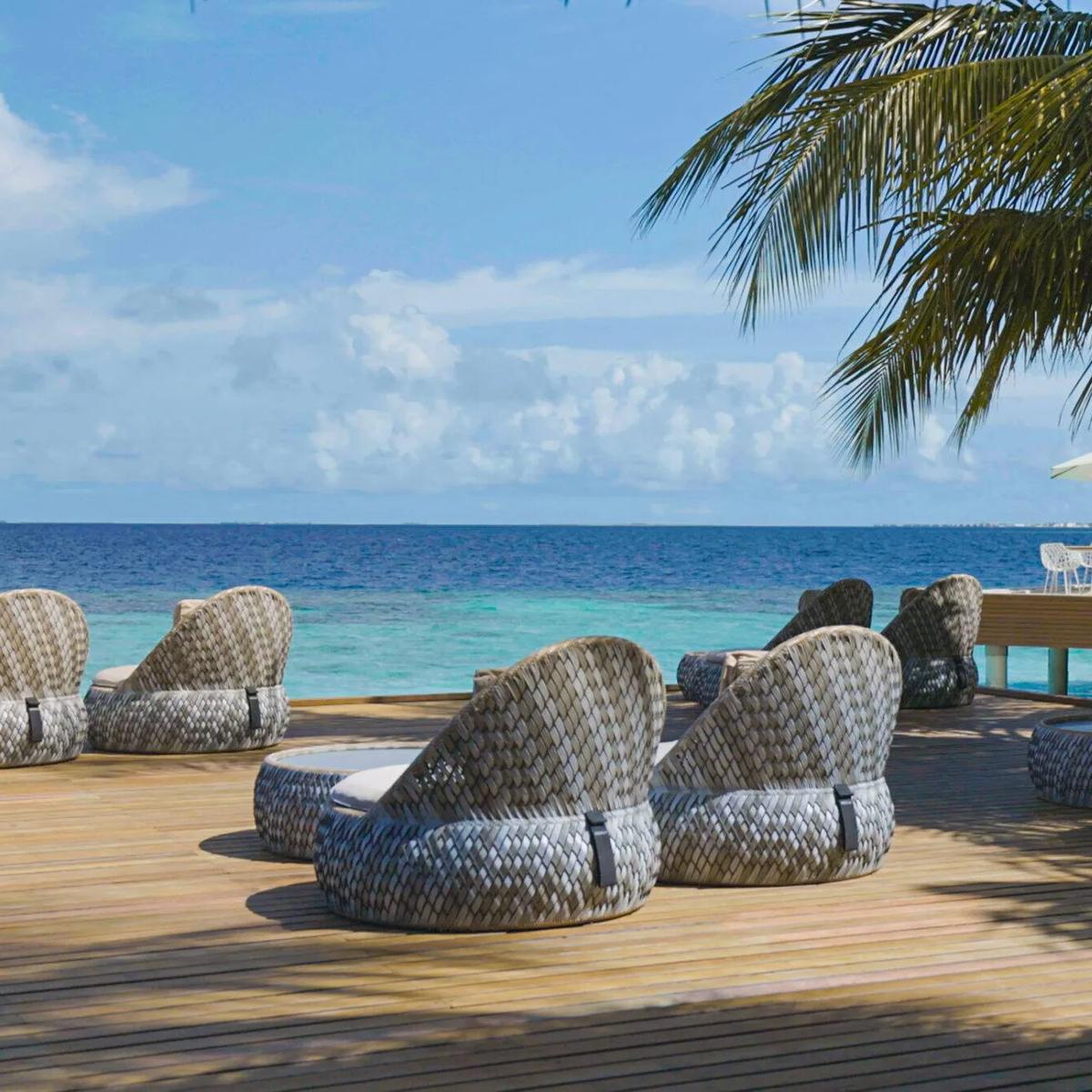 Woven daybeds and loungers arranged on Umbar's beachfront deck under a palm tree