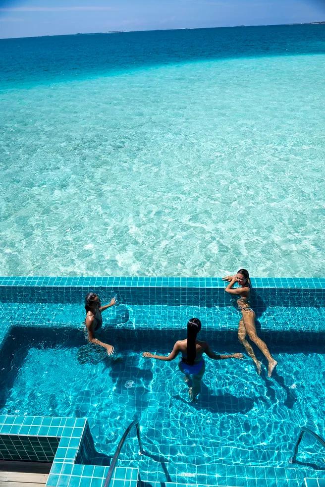 Three guests standing in a tiled hydro pool that appears to merge with the open lagoon beyond