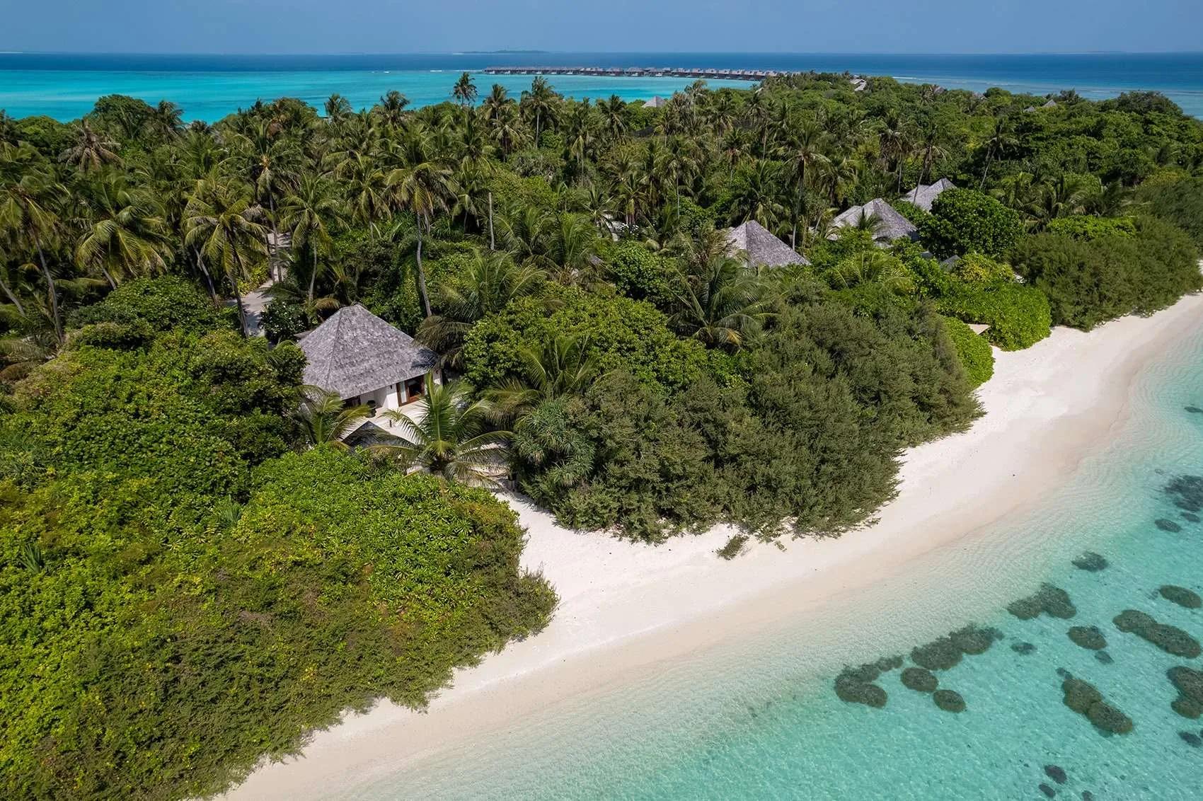 Exterior of a Sunset Beach Villa at Hideaway, its thatched roof set among coconut palms on the private beach