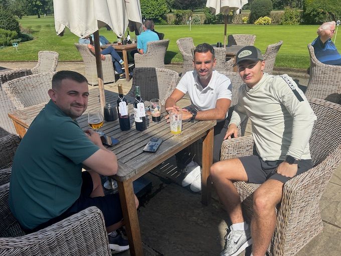 Three members at a terrace table with the course behind
