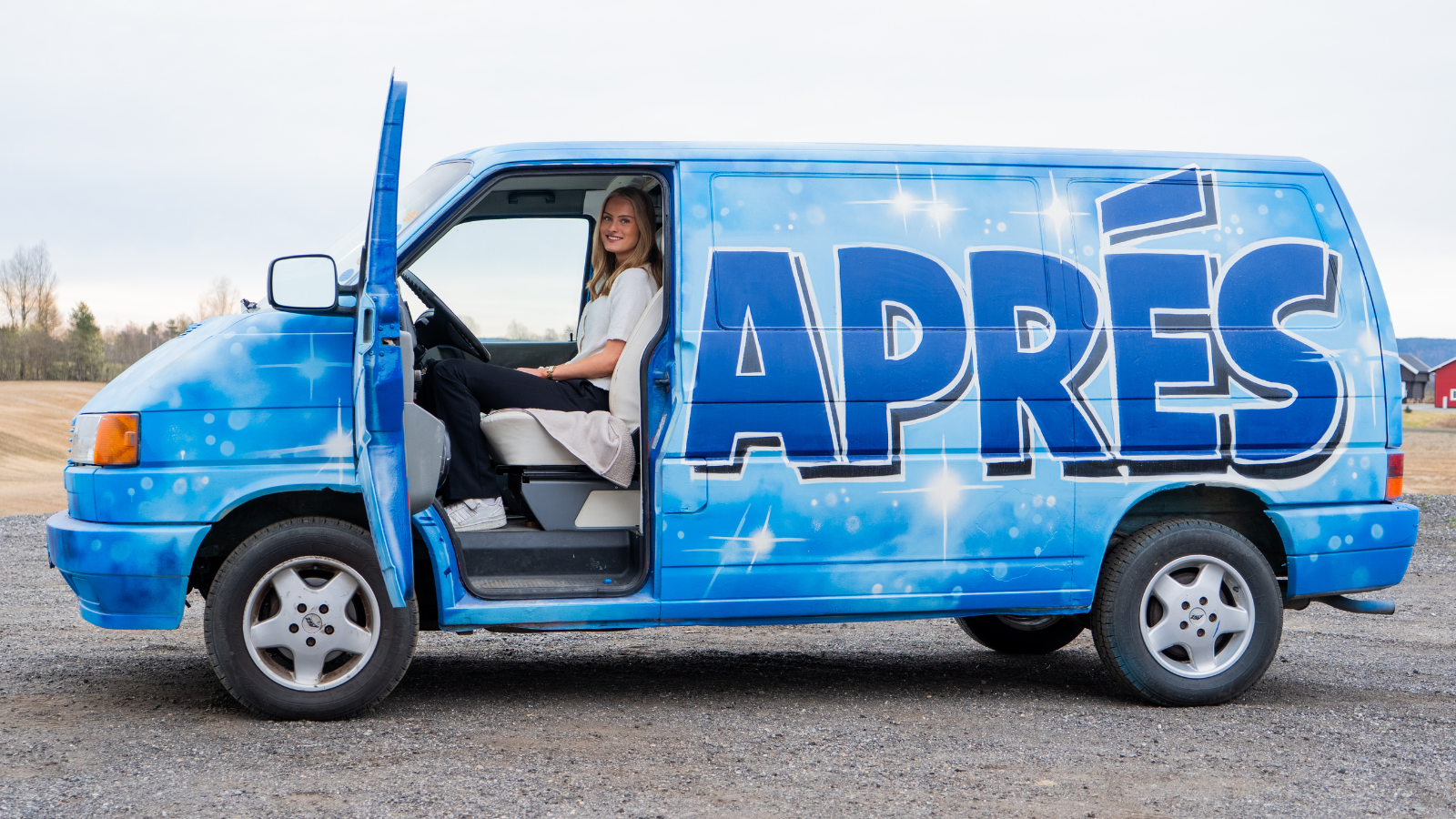 Bildet viser en russ som stolt viser frem den lyseblåe vanen sin. APRÉS står i store mørkeblåe bokstaver på siden av bilen.
