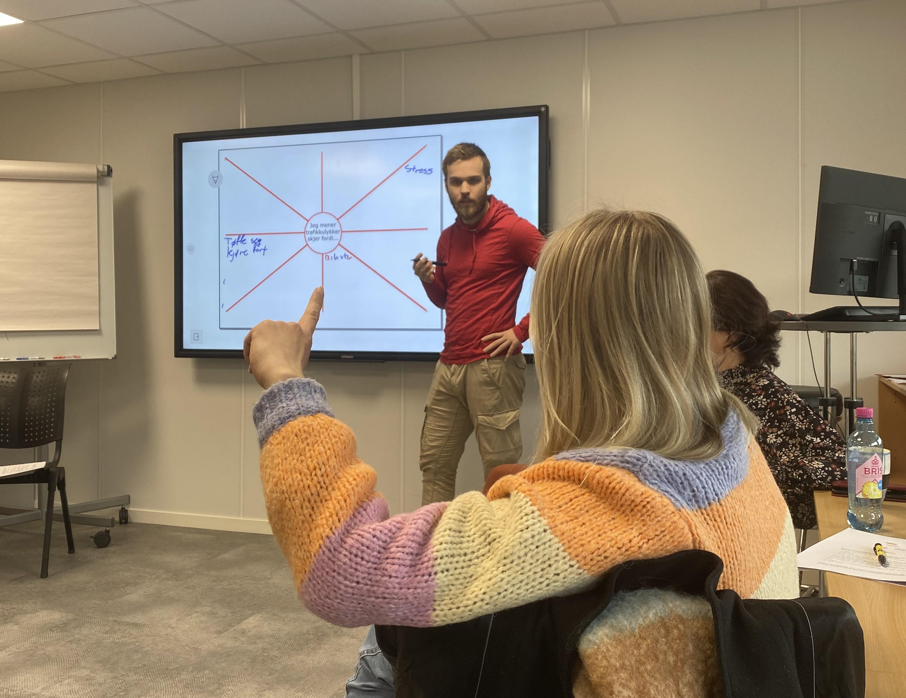 Bilde viser Trafikklærerstudent Lars Gunnar Heimstad Rambjør som står foran storskjerm med tankekartet. Kine Osan fra Trafikkforum vises i front og rekker opp hånda for å svare på spørsmål.