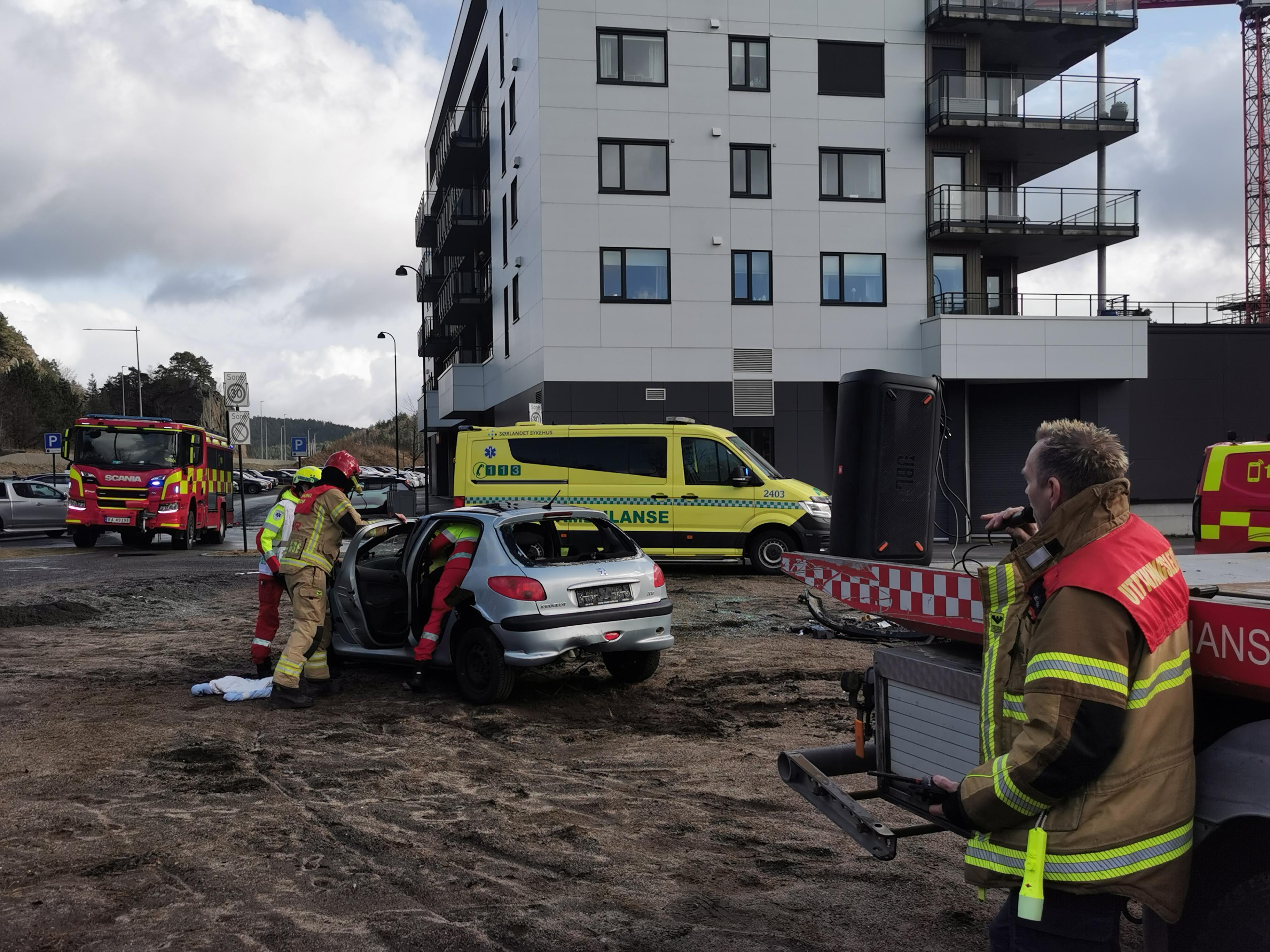 Bildet viser en rød brannbil og en gul ambulansebil i bakgrunn. Foran ser vi den sølve bilen fra droppet, og brannvesen som prøver å få ut personen.