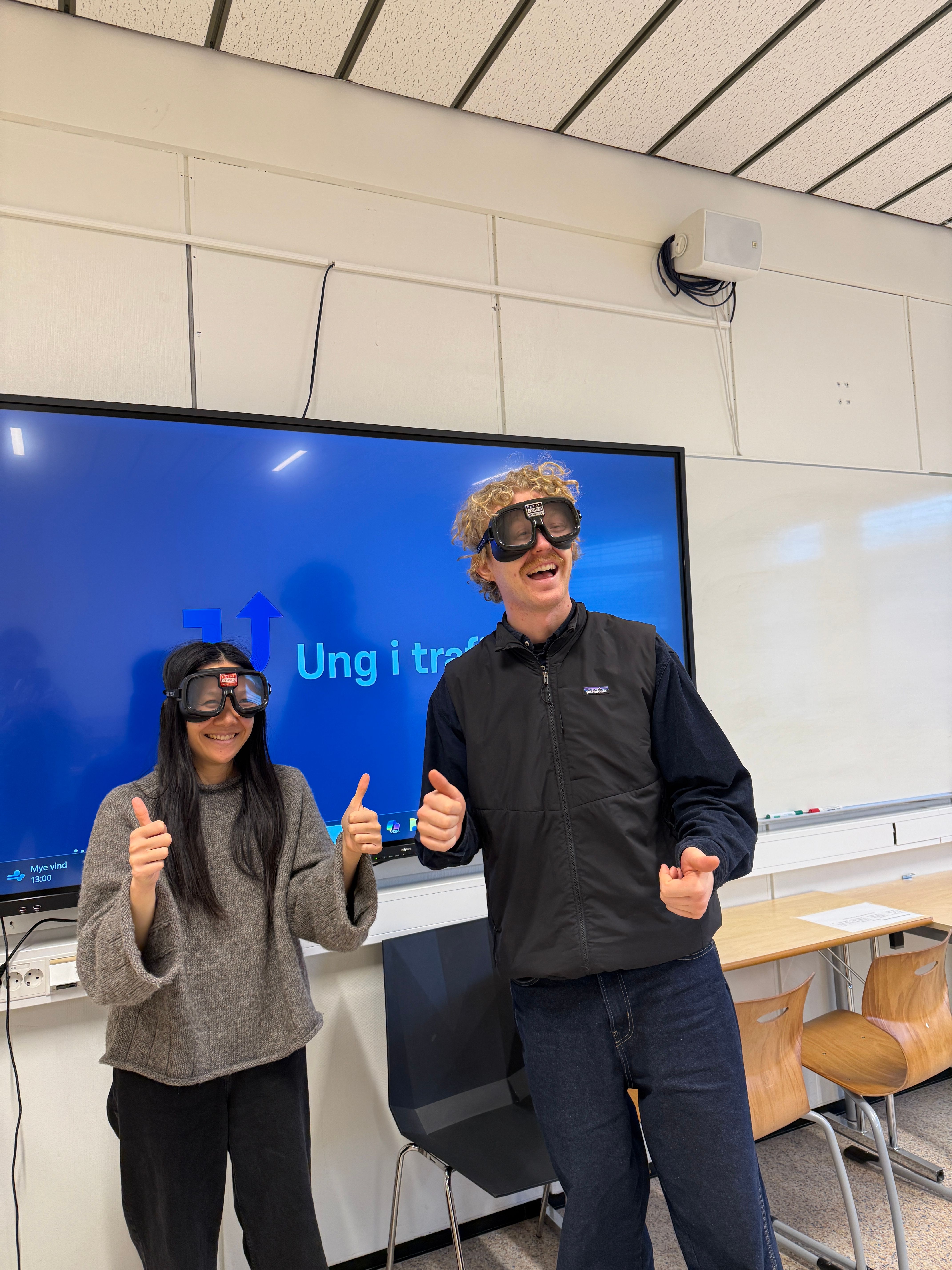 Johannes og Lan fra Ung i trafikken står i et klasserom med promillebriller på. 