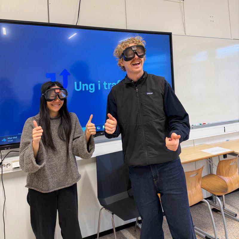 Johannes og Lan fra Ung i trafikken står i et klasserom med promillebriller på.
