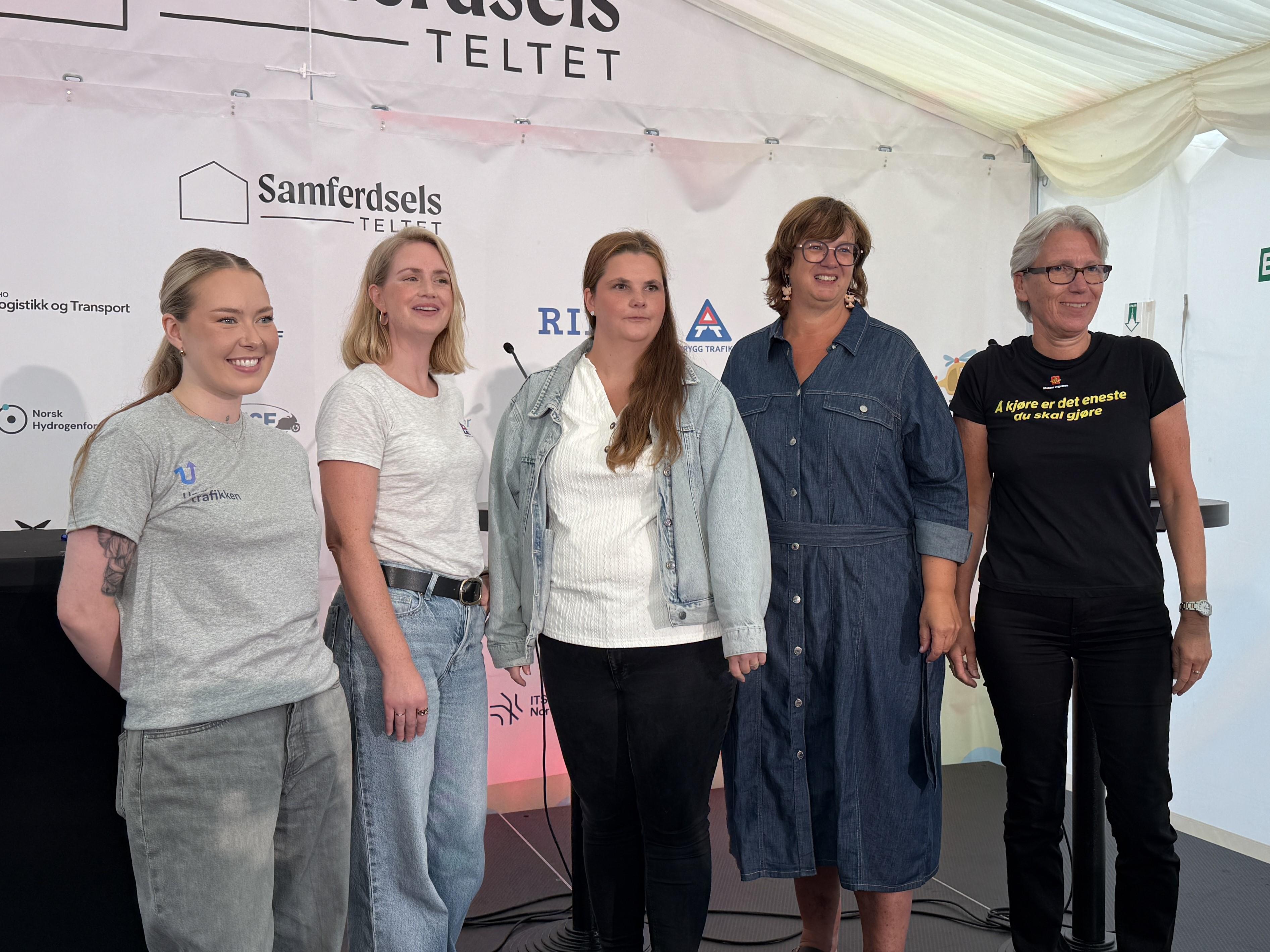 Bildet viser 5 kvinner stå ved siden av hverandre i et hvitt telt på en svart scene. De smiler til kamera.