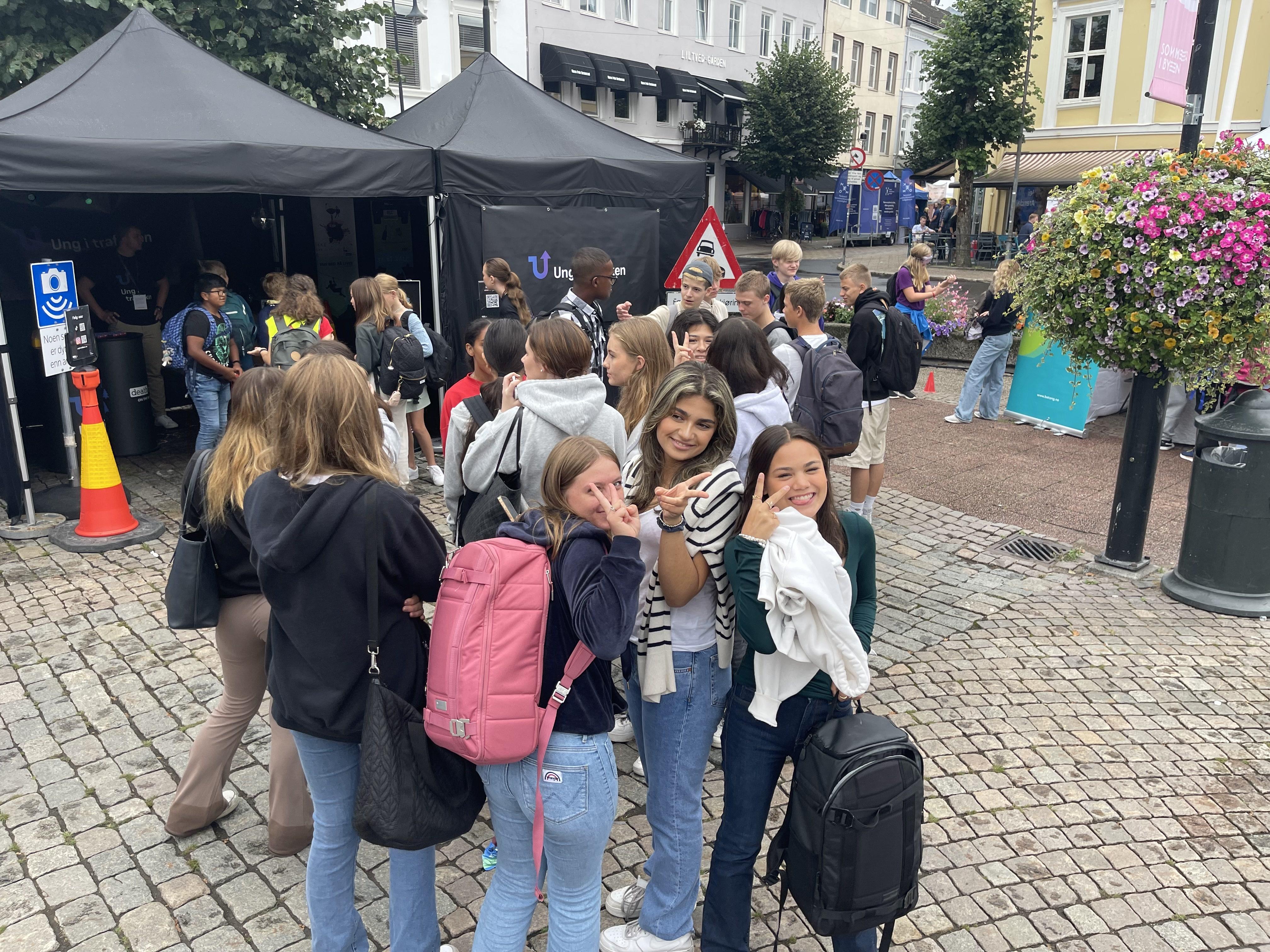 Bilde av området rundt standen og publikum. Jentegjeng i front med peace-tegn smiler til kamera.