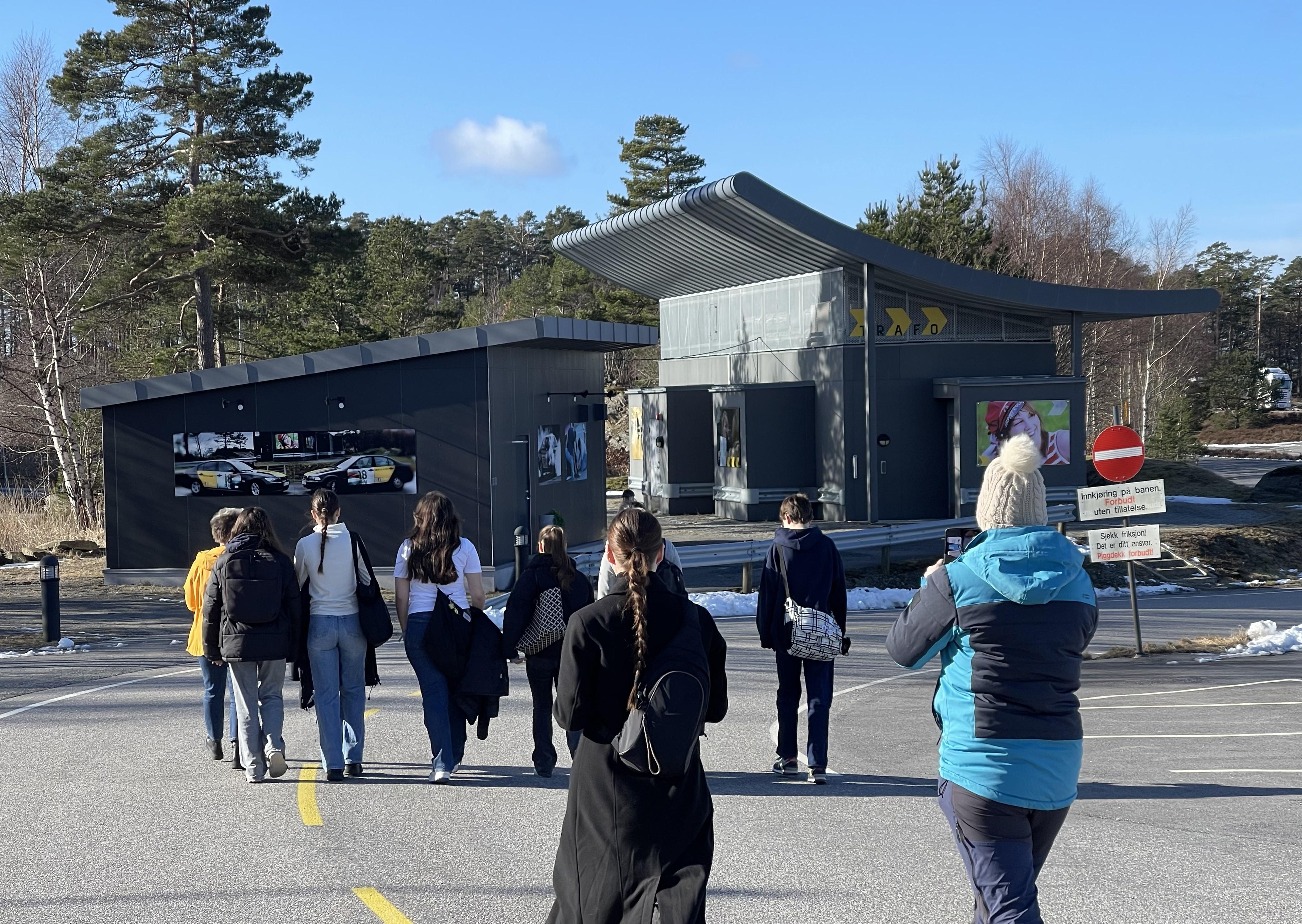Bildet viser Trafo-byggene i grå farge og skrått tak med bilder utenpå, blå himmel, og ungdom gående på vei til byggene.