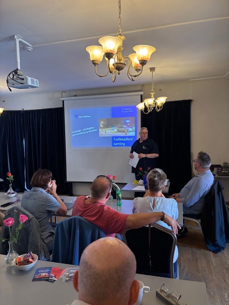 Bildet viser tre personer som ser på foredragsholder og daglig leder i ung i trafikken stig eid sandstad, som står foran en skjerm med en powerpoint med tittel: velkommen til trafikkatferd 2026.