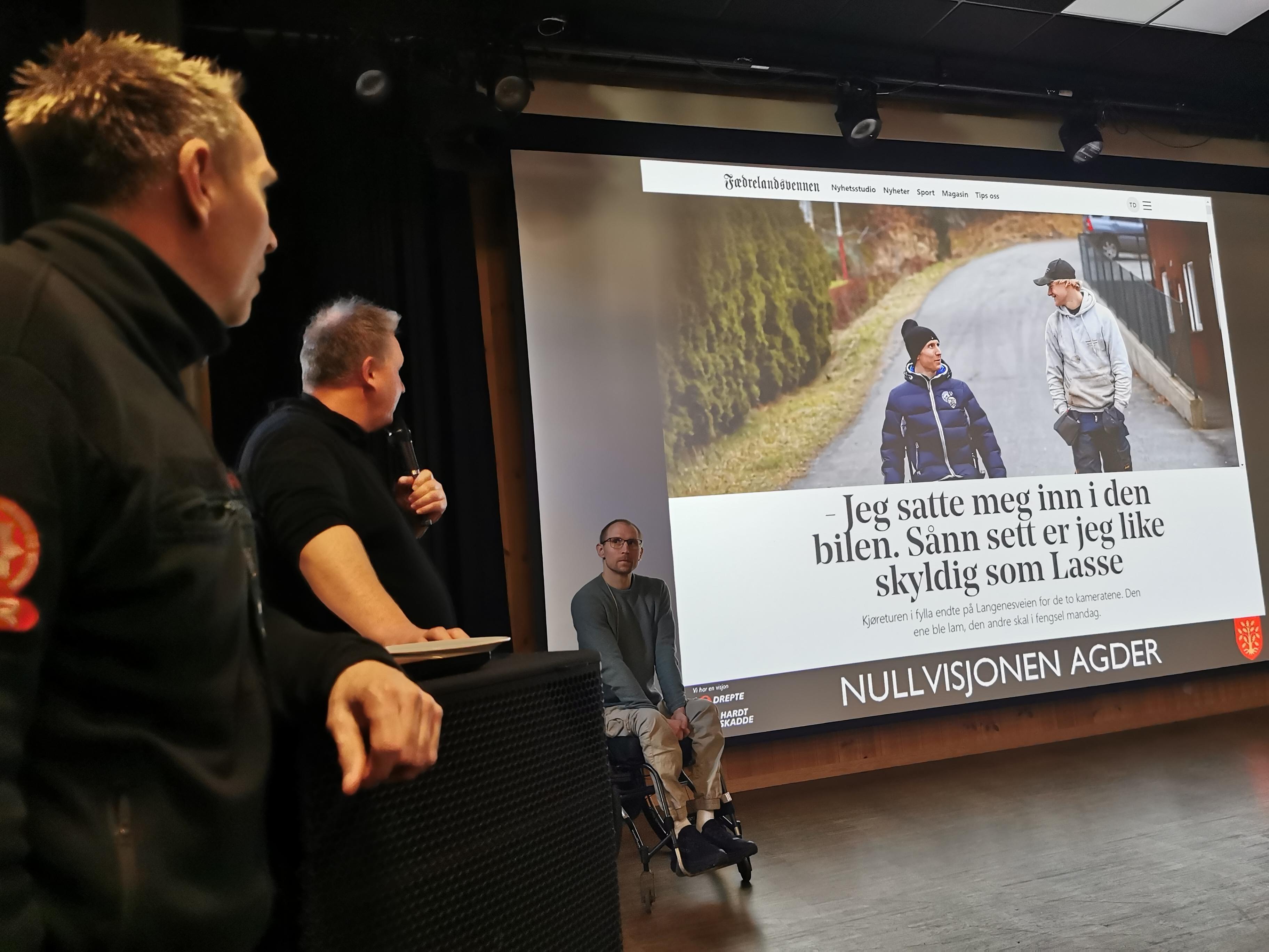 På bildet ser vi i front, to menn fra nullvisjonen Agder. I bakgrunn ser vi en stor skjerm med et skjermbilde fra en avis med tittelen: "- Jeg satte meg inn i den bilen. Sånn sett er jeg like skyldig som Lasse." Foran skjermen og på scenen sitter Henrik i rullestol.