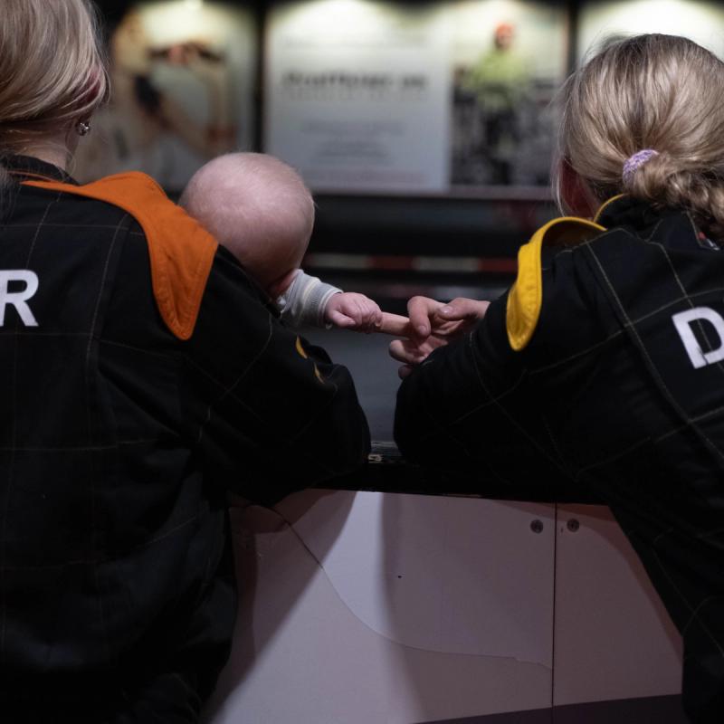 To kvinner og en baby på en gocart-bane. De ser på de som kjører.