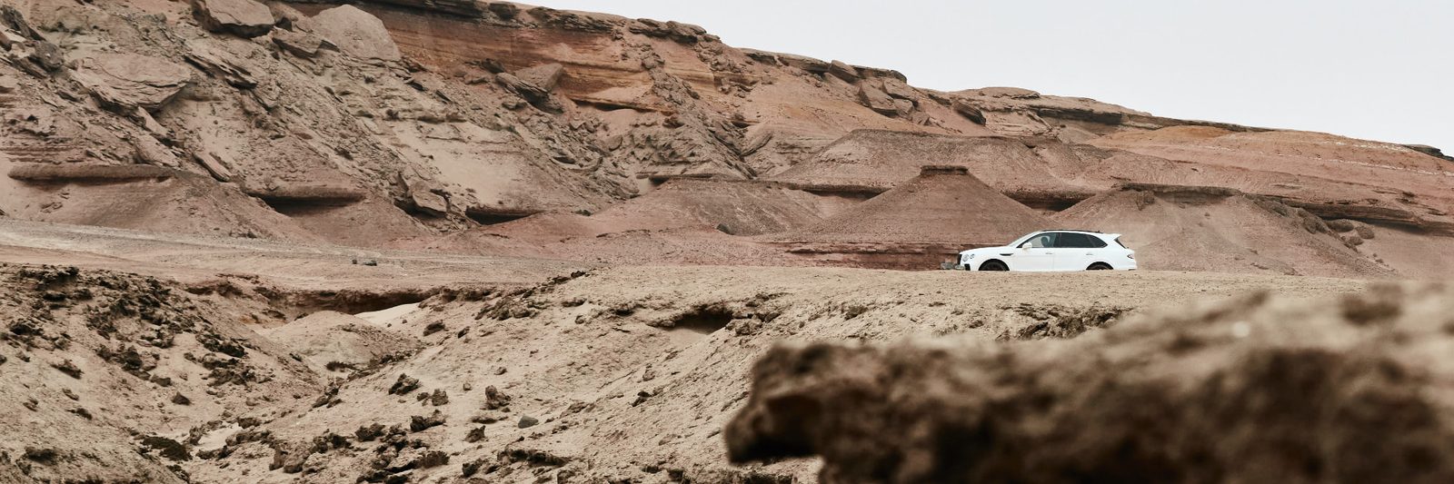 White Bentley Bentayga parked against layered red rock desert hills