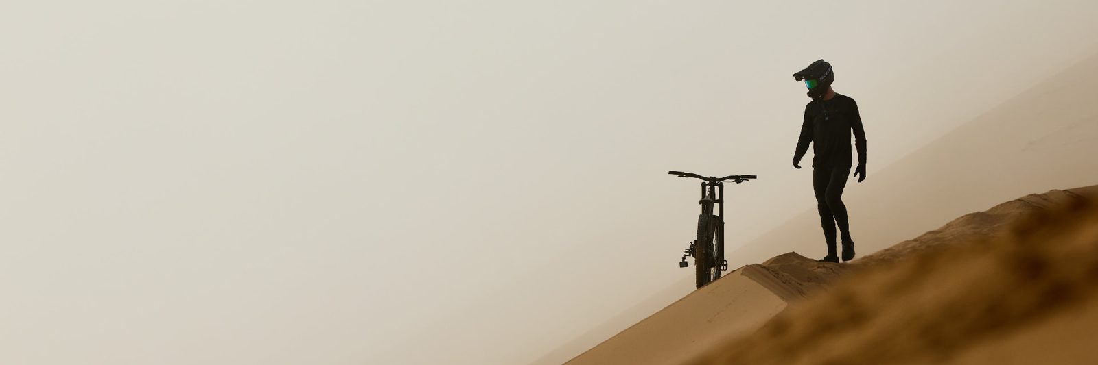 Cyclist standing beside a mountain bike on the crest of a hazy desert dune