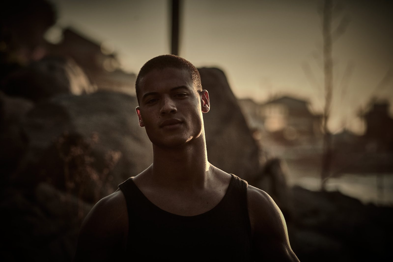 Athletic young man in a dark tank top at golden hour, rim-lit against rugged rocks