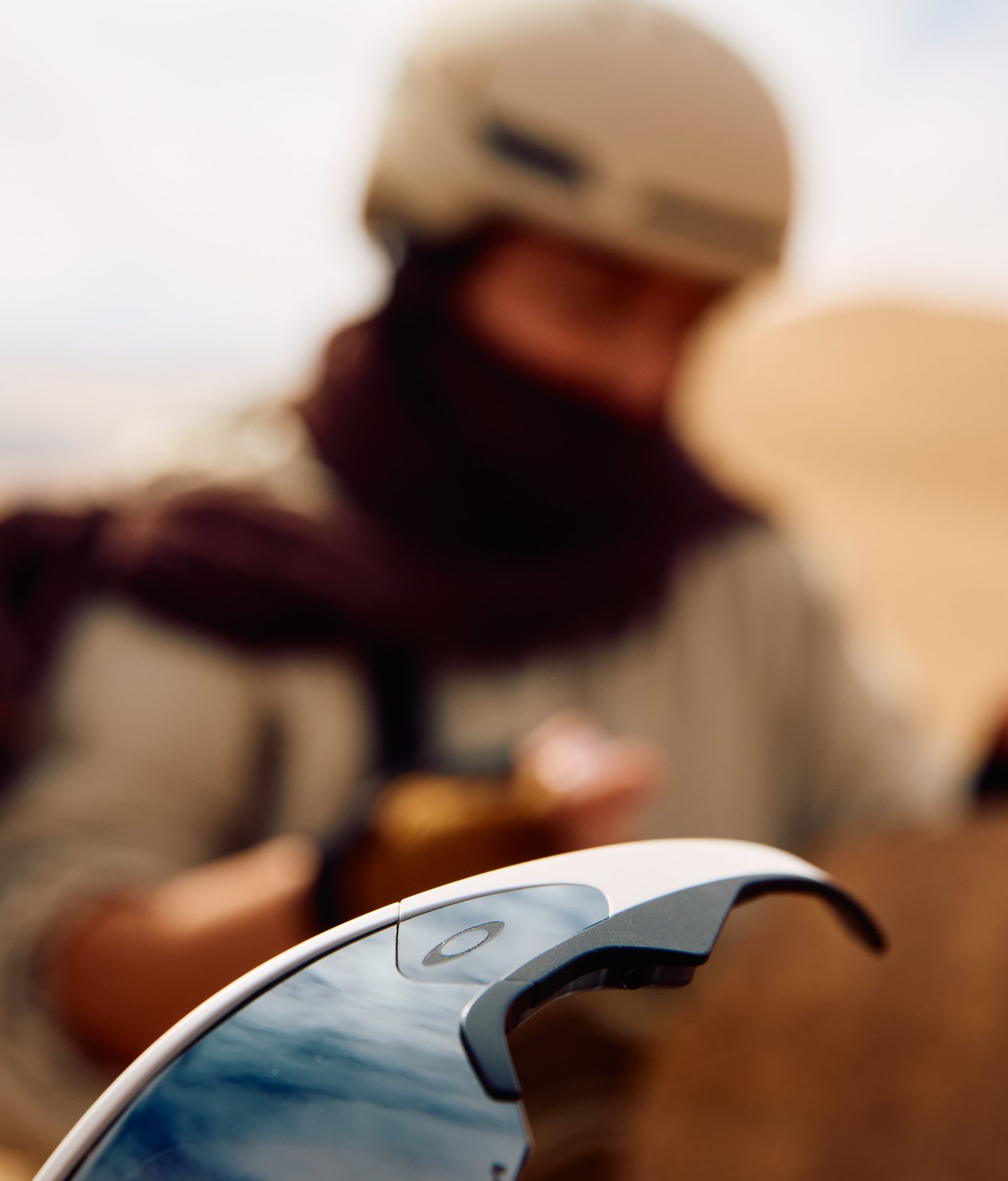 Close-up of reflective sport goggles with an athlete seated in soft focus on desert sand