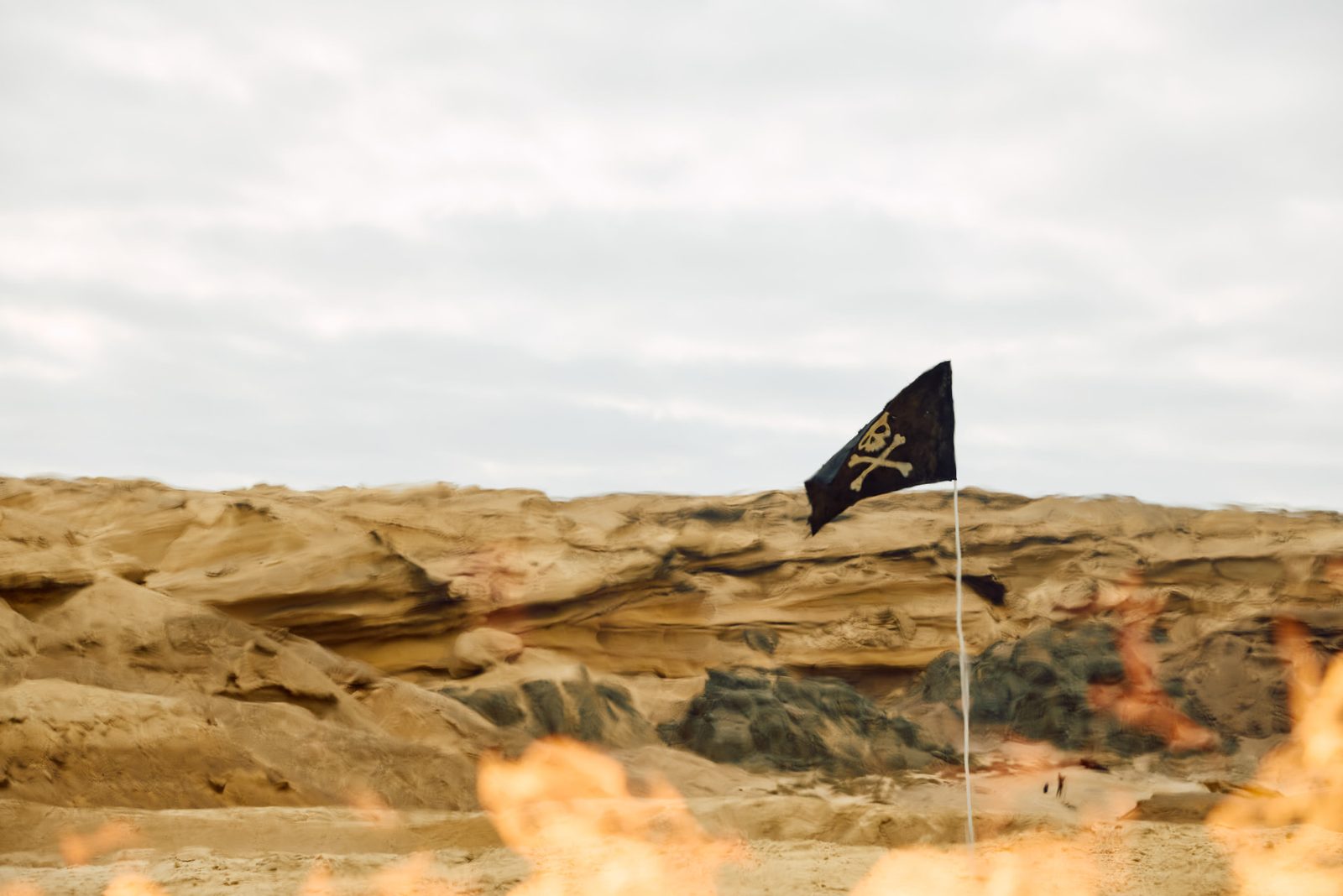 Black pirate flag flying from a thin pin above eroded sandstone formations, orange flame blurred in the foreground