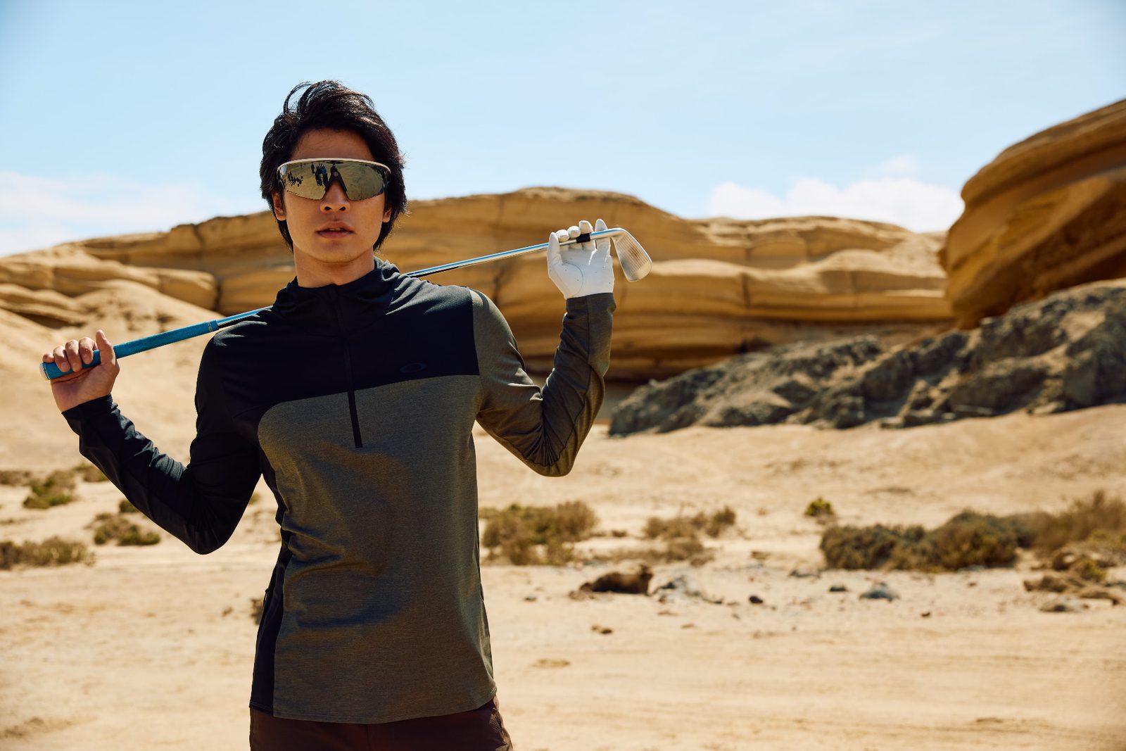 Golfer in a white glove resting a club behind his neck, posed against layered desert rock