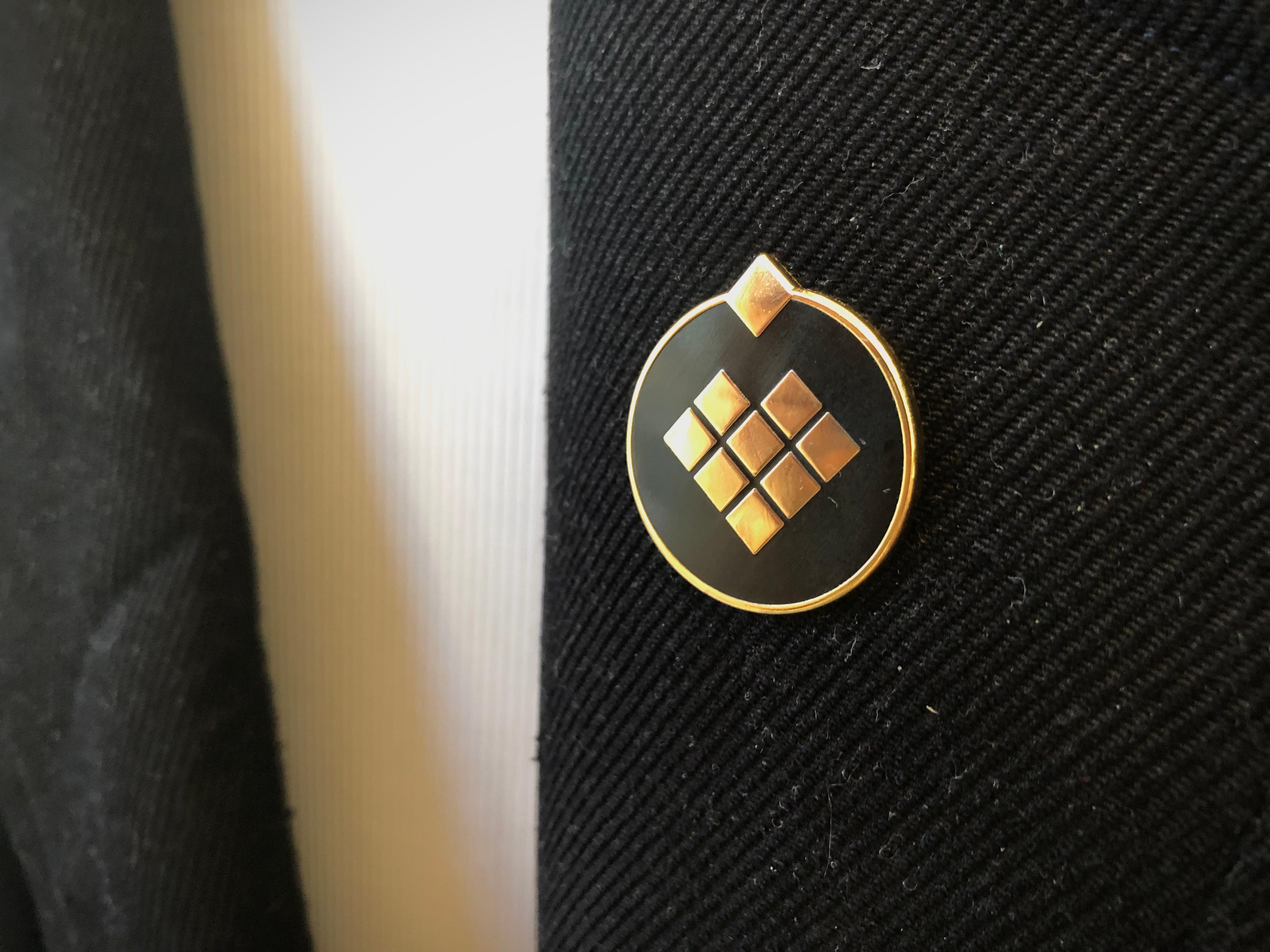 Black and gold enamel pin with the Giving What We Can logo in the centre