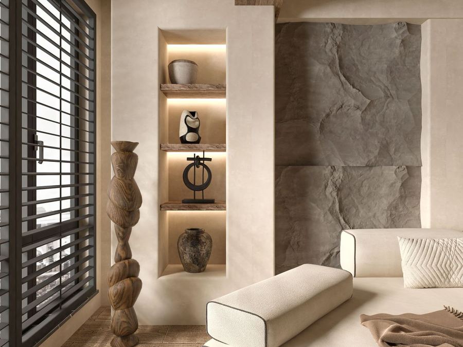 Lime-plastered wall with lit niches holding ceramics, beside a textured stone feature and a linen daybed