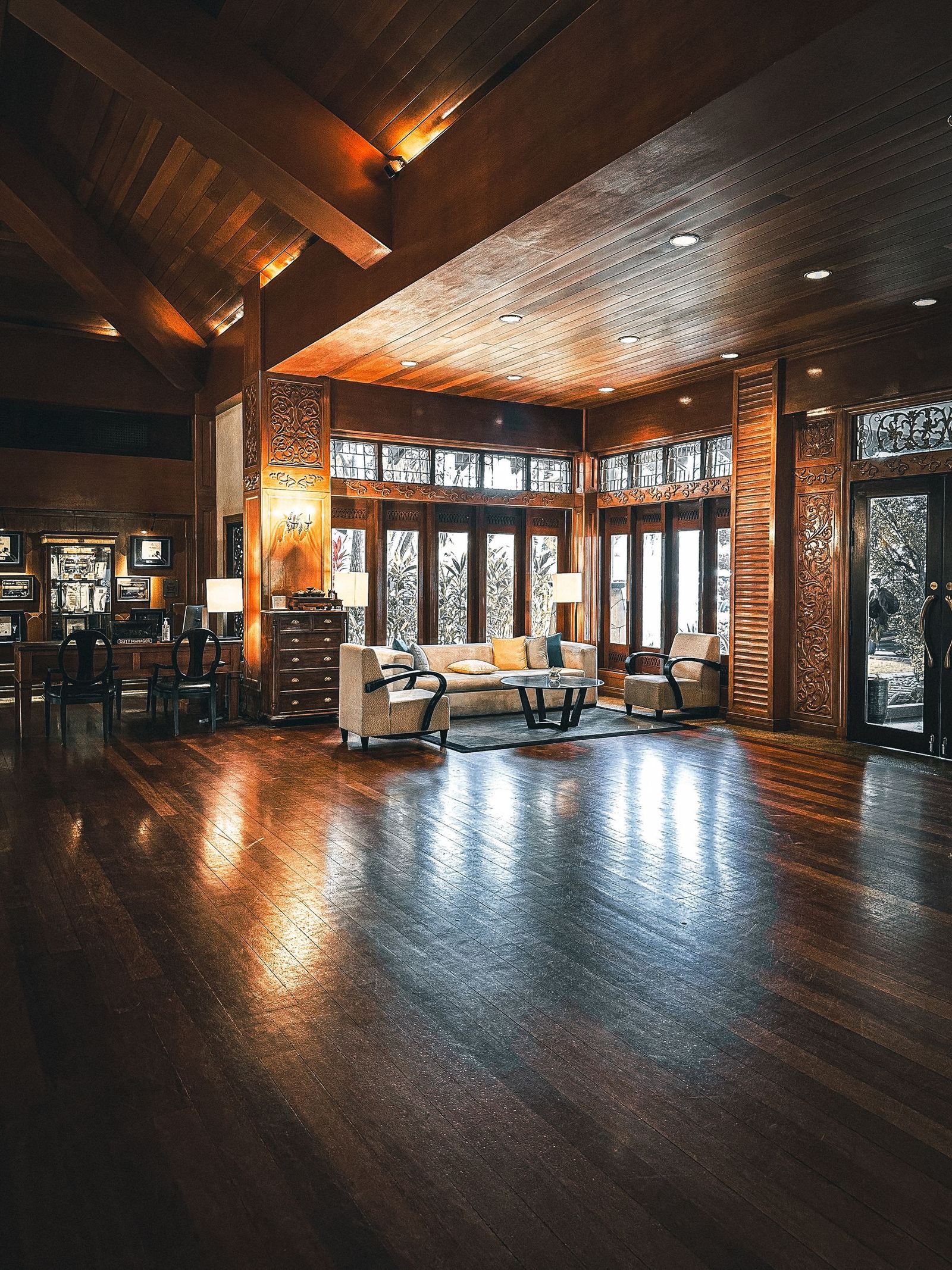 A warm timber-lined living room at dusk, lamps glowing against dark wood panelling