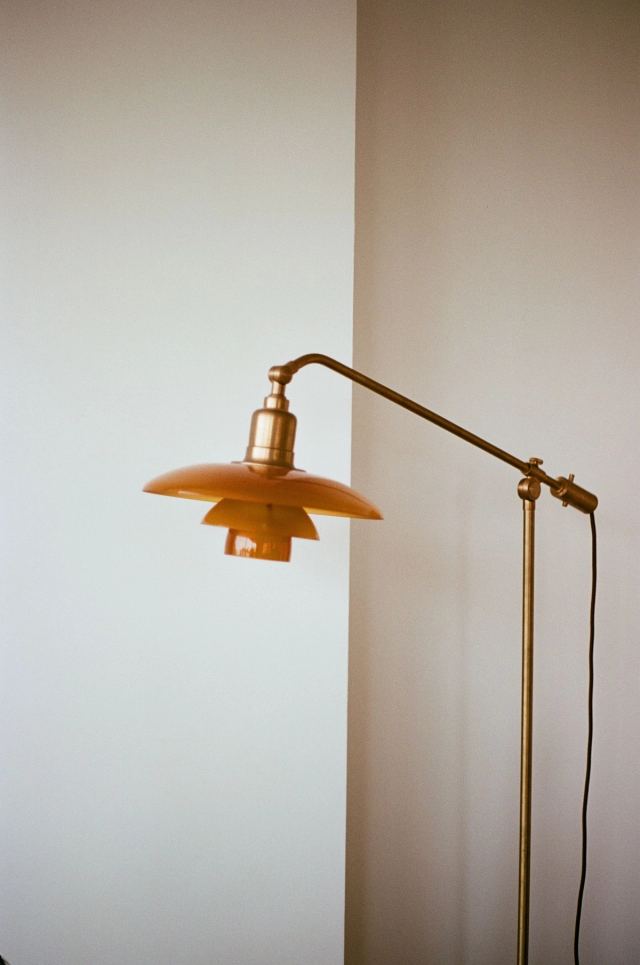 Brass floor lamp with an amber shade against a pale plaster wall