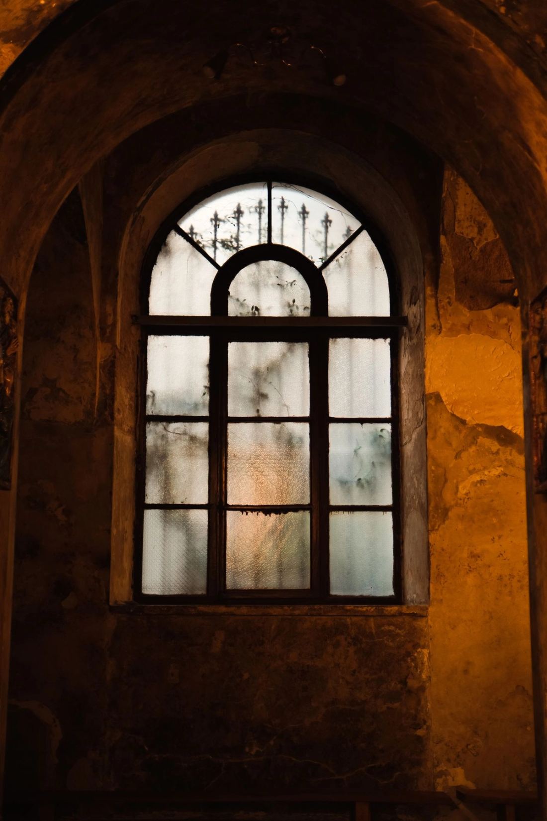 Tall arched window framed by raw stone and warm plaster