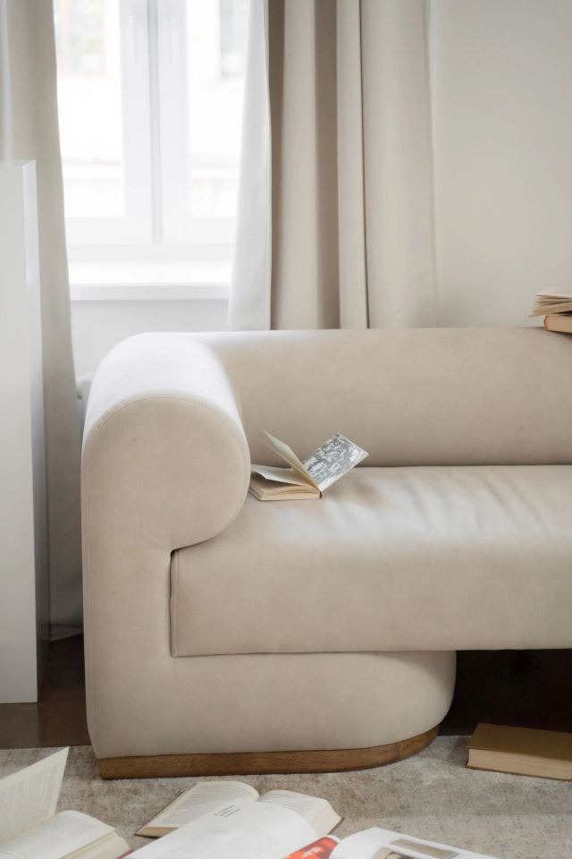 Curved cream boucle sofa beside linen curtains, an open book on the seat