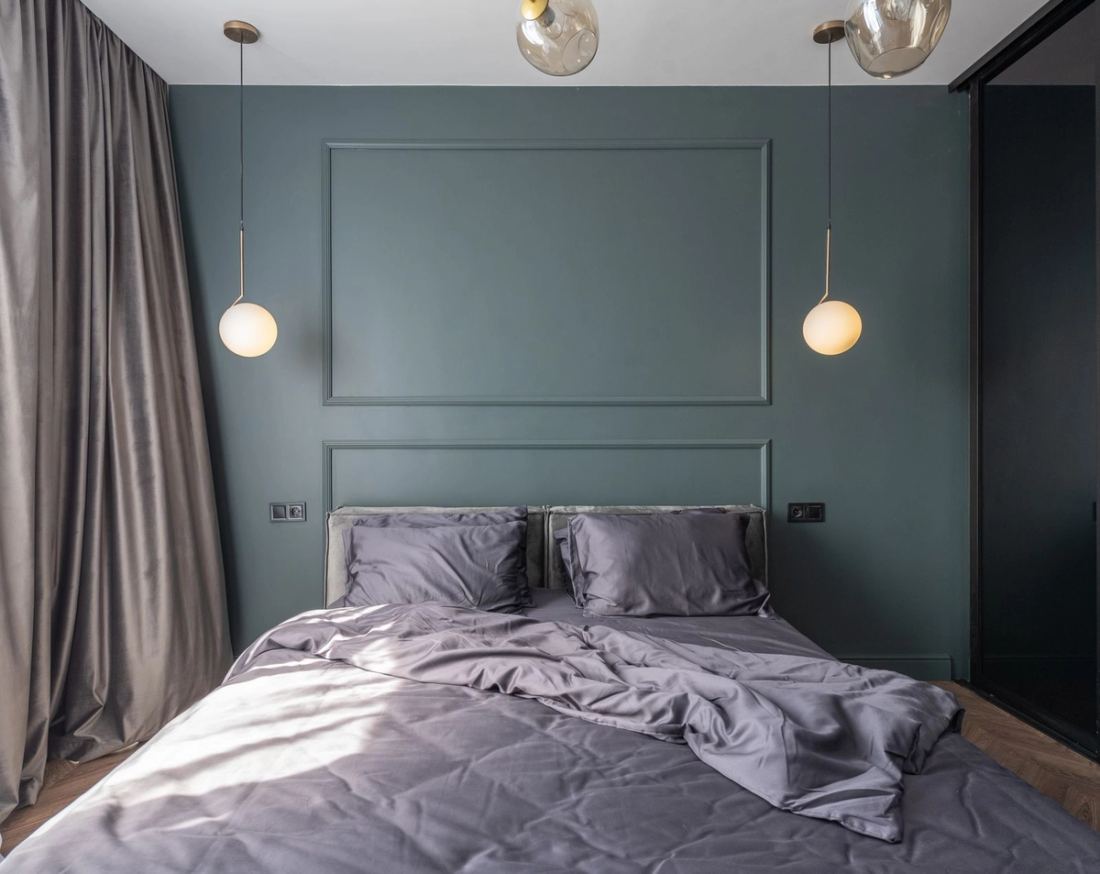 Bedroom with a deep green wall, brass pendant and grey linen