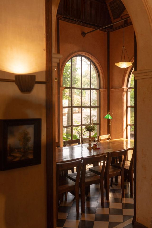 Dining nook beneath a tall arched window in warm timber, with a checkerboard floor