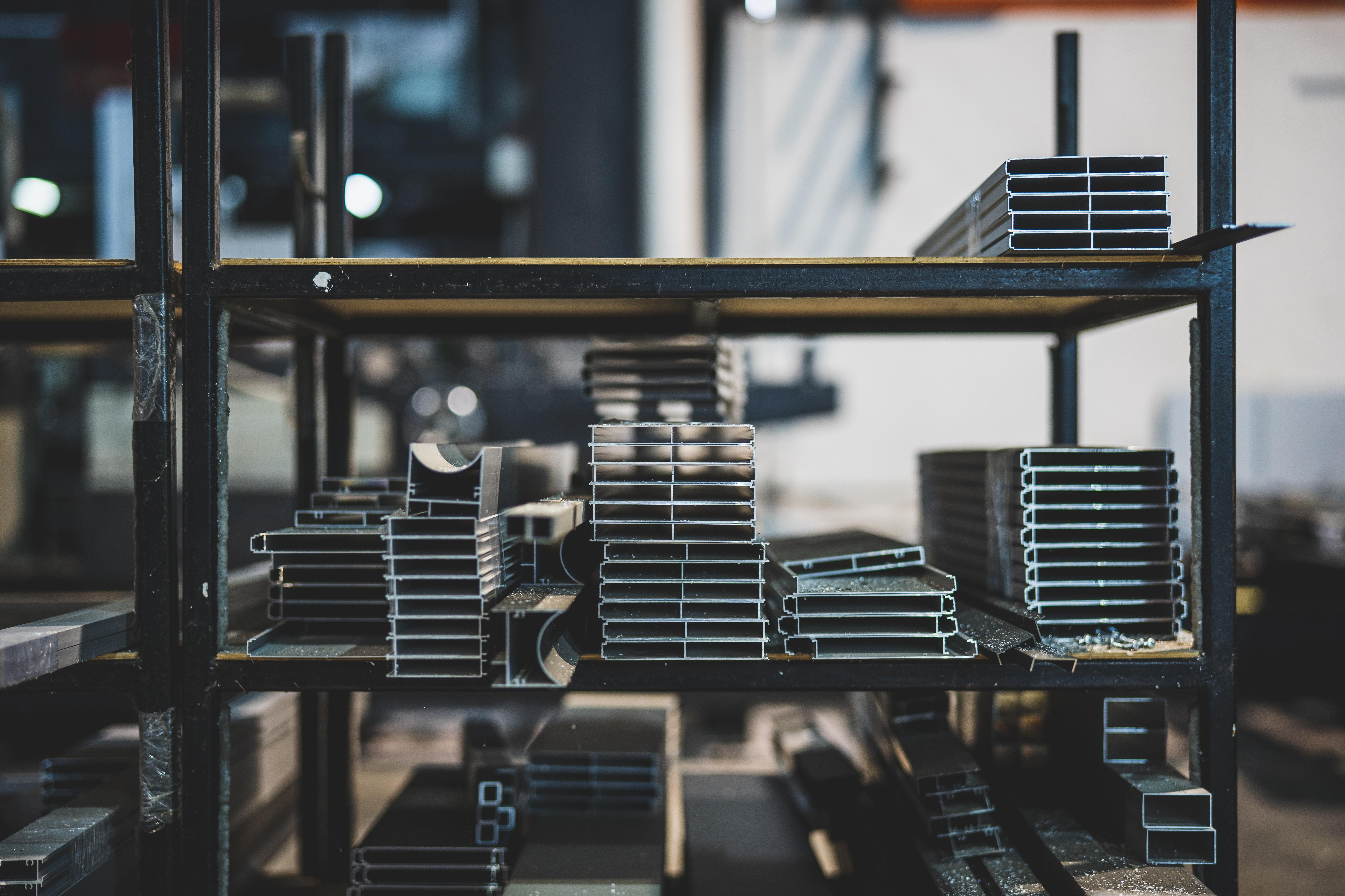 Stacked aluminium and steel profiles on shelving inside a metal fabrication workshop