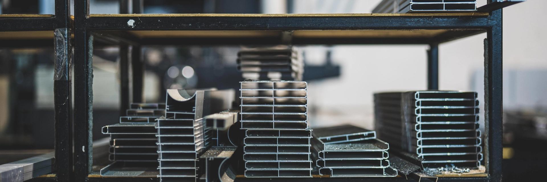 Stacked aluminium and steel profiles on shelving inside a metal fabrication workshop