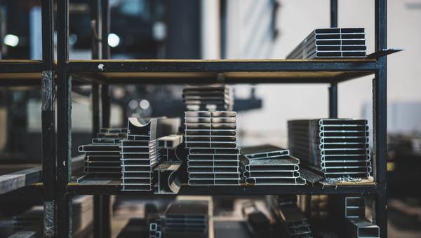 Stacked aluminium and steel profiles on shelving inside a metal fabrication workshop