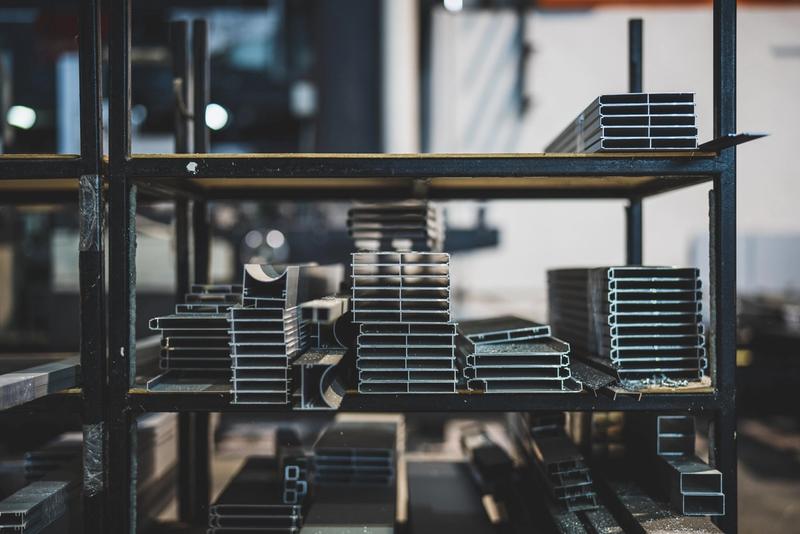 Stacked aluminium and steel profiles on shelving inside a metal fabrication workshop