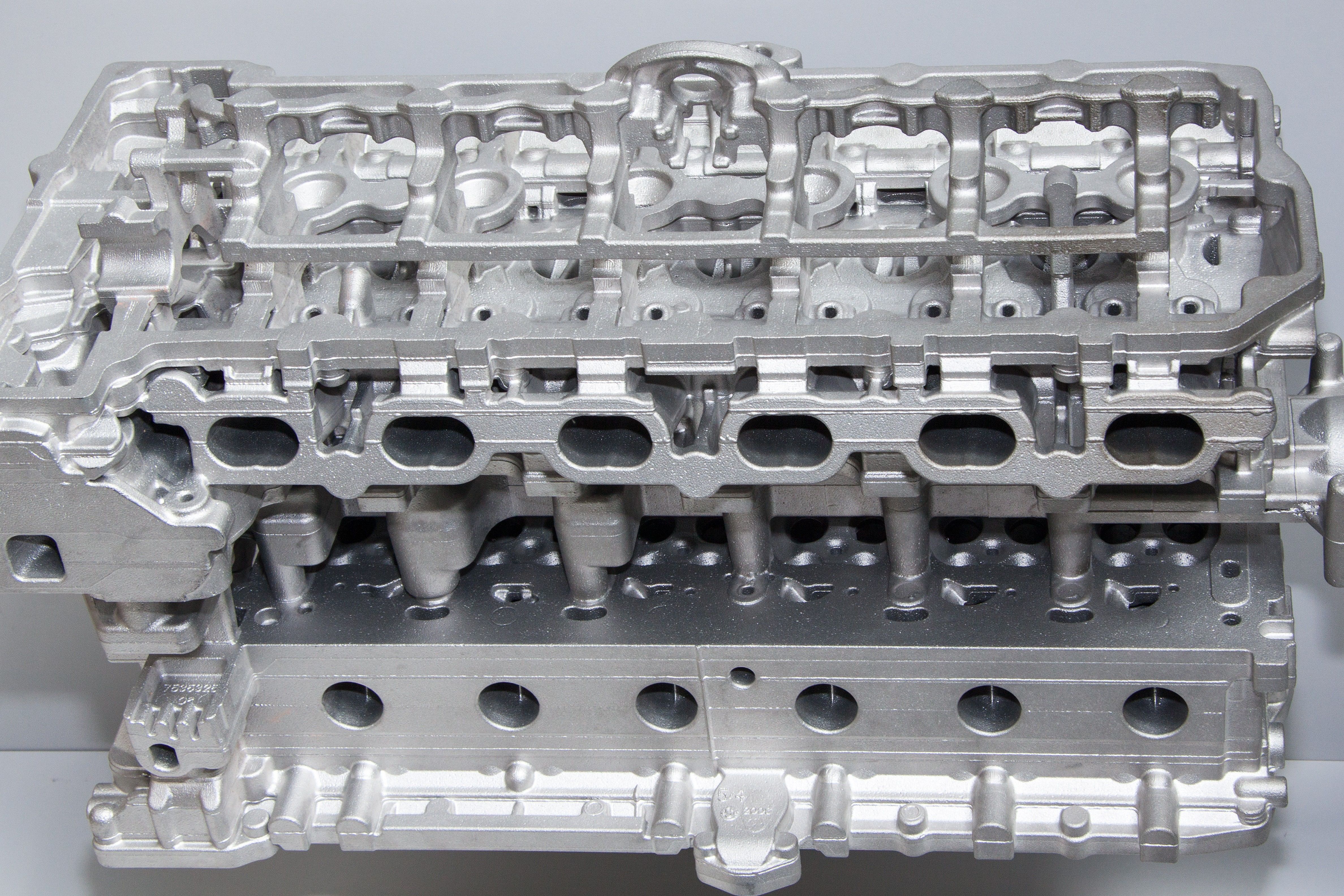 Bare aluminum die cast cylinder head showing intricate cast features and machined surfaces