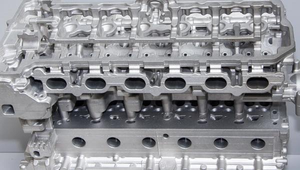 Bare aluminum die cast cylinder head showing intricate cast features and machined surfaces