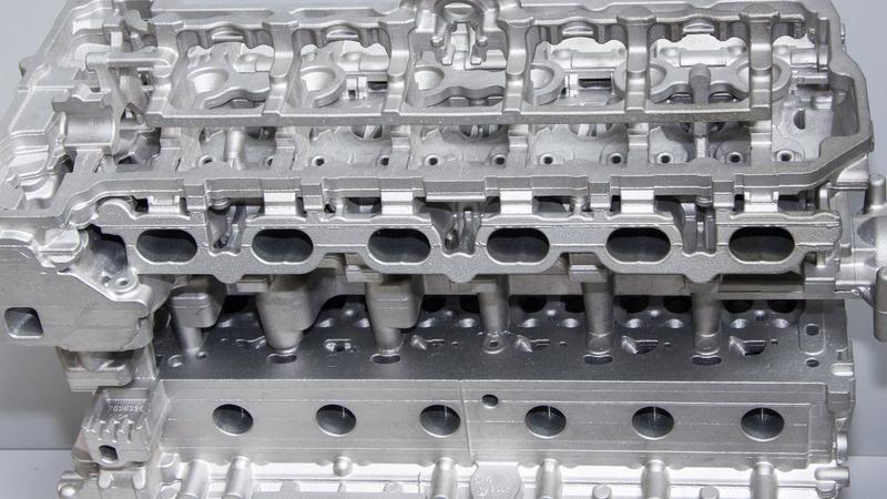 Bare aluminum die cast cylinder head showing intricate cast features and machined surfaces