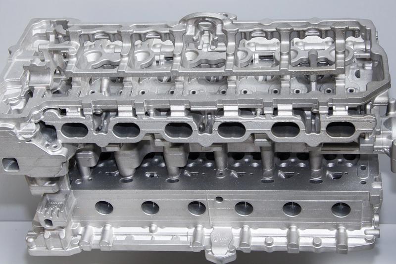 Bare aluminum die cast cylinder head showing intricate cast features and machined surfaces