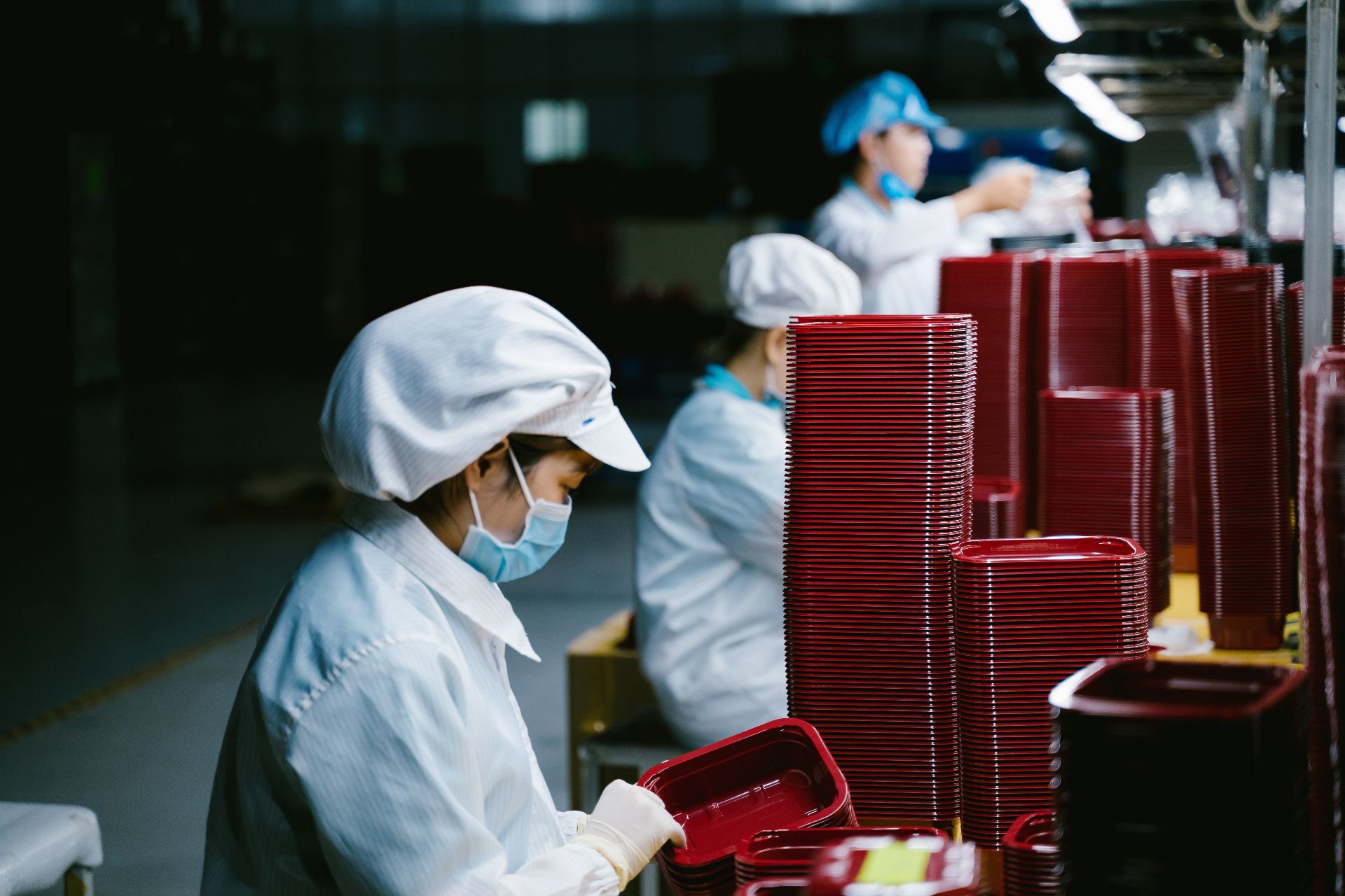 Workers in a plastic injection molding production line stacking red moulded trays in a Vietnam factory.