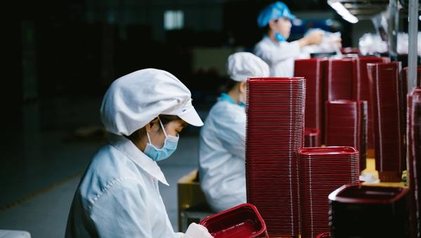 Workers in a plastic injection molding production line stacking red moulded trays in a Vietnam factory.